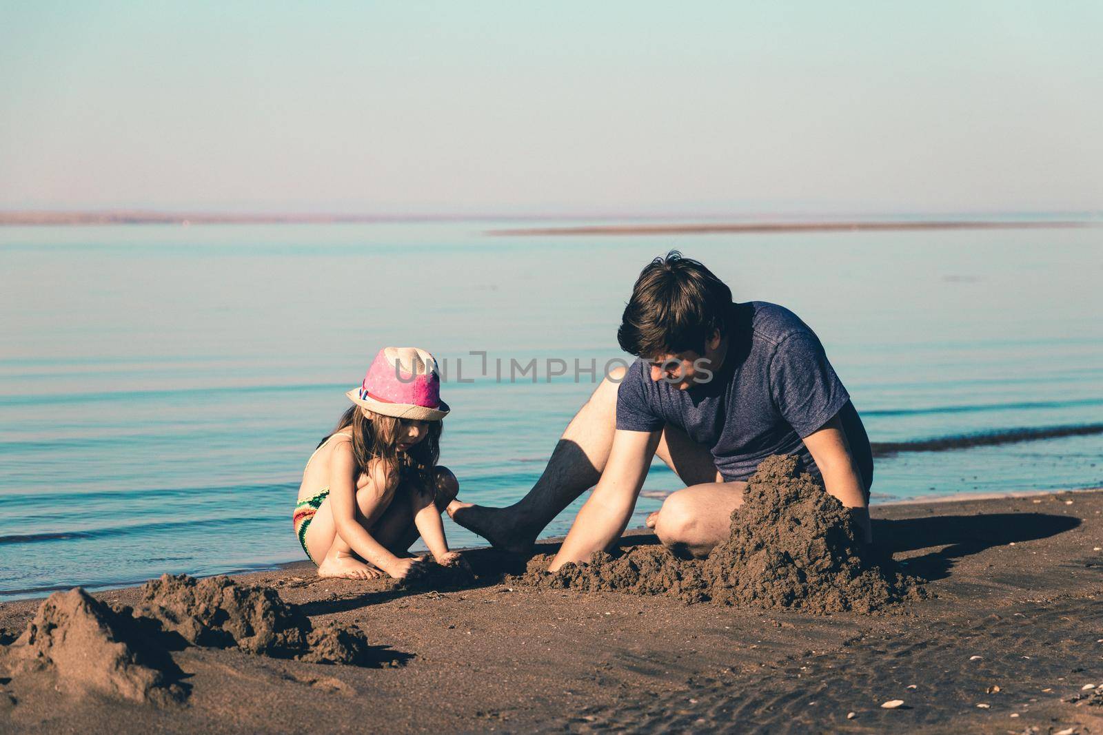 Father and his daughter build sand castles on the beach. Toned lifestyle photo.