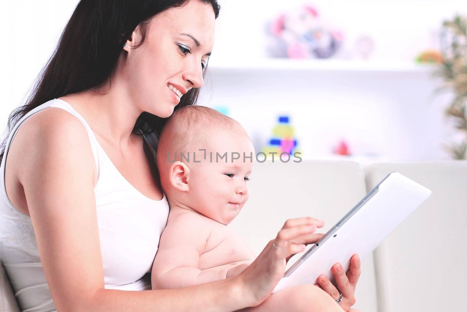 mother and baby child are looking to play and read tablet computer on the couch at home