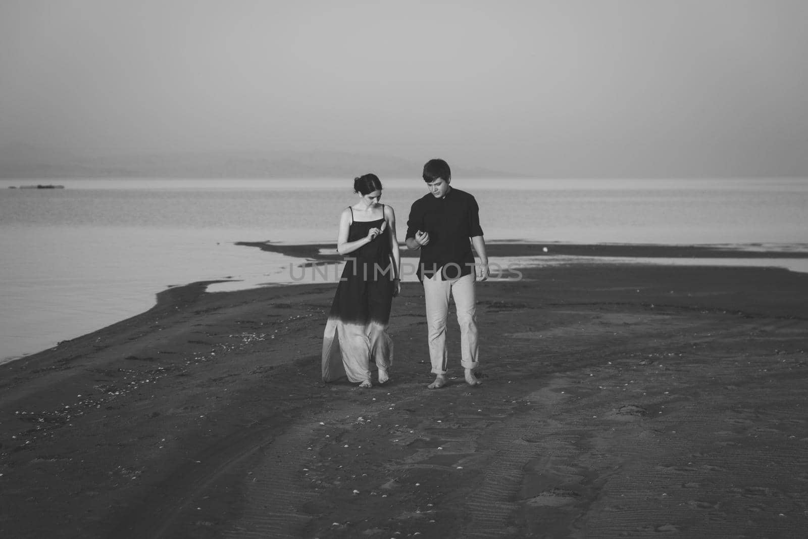 Black and white portrait of young couple of lovers walking along the evening beach. Copy space.