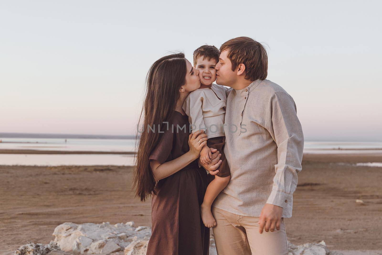 Family look of natural linen clothing on the evening beach. Young family hugs and kisses.