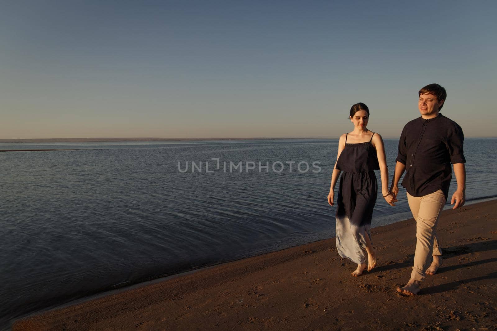 Young couple of lovers walking along the evening beach. Copy space.