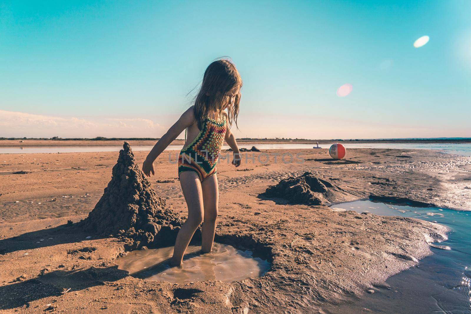 Little cute girl in a knitted swimsuit playing with sand on the seashore.