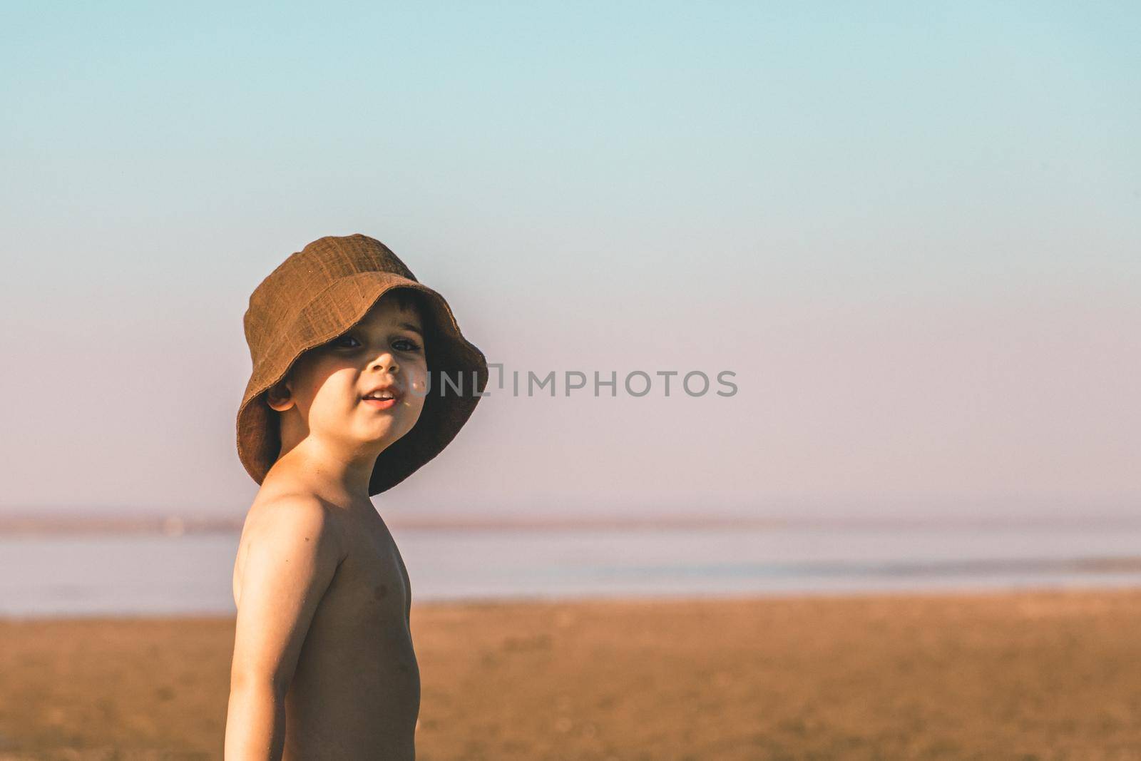 Portrait of a little boy 3 years old in a brown panama hat on the beach by Rom4ek