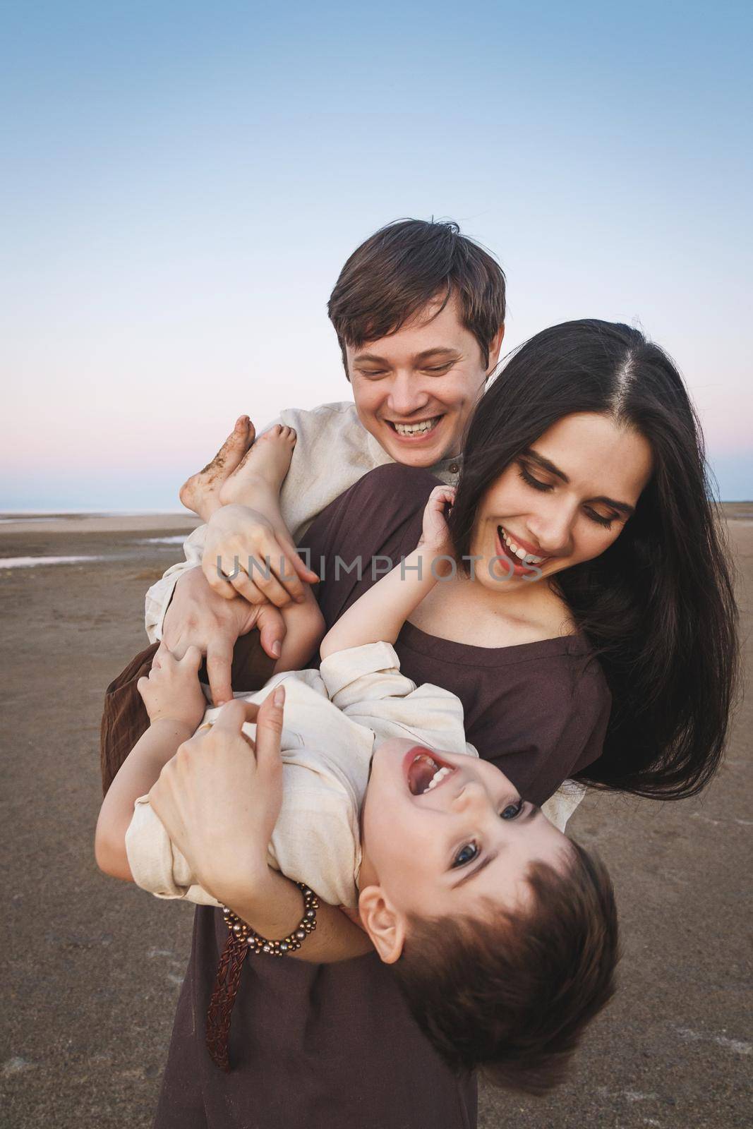 Happy laughing young family vertical portrait on the evening beach. Family look linen clothes.