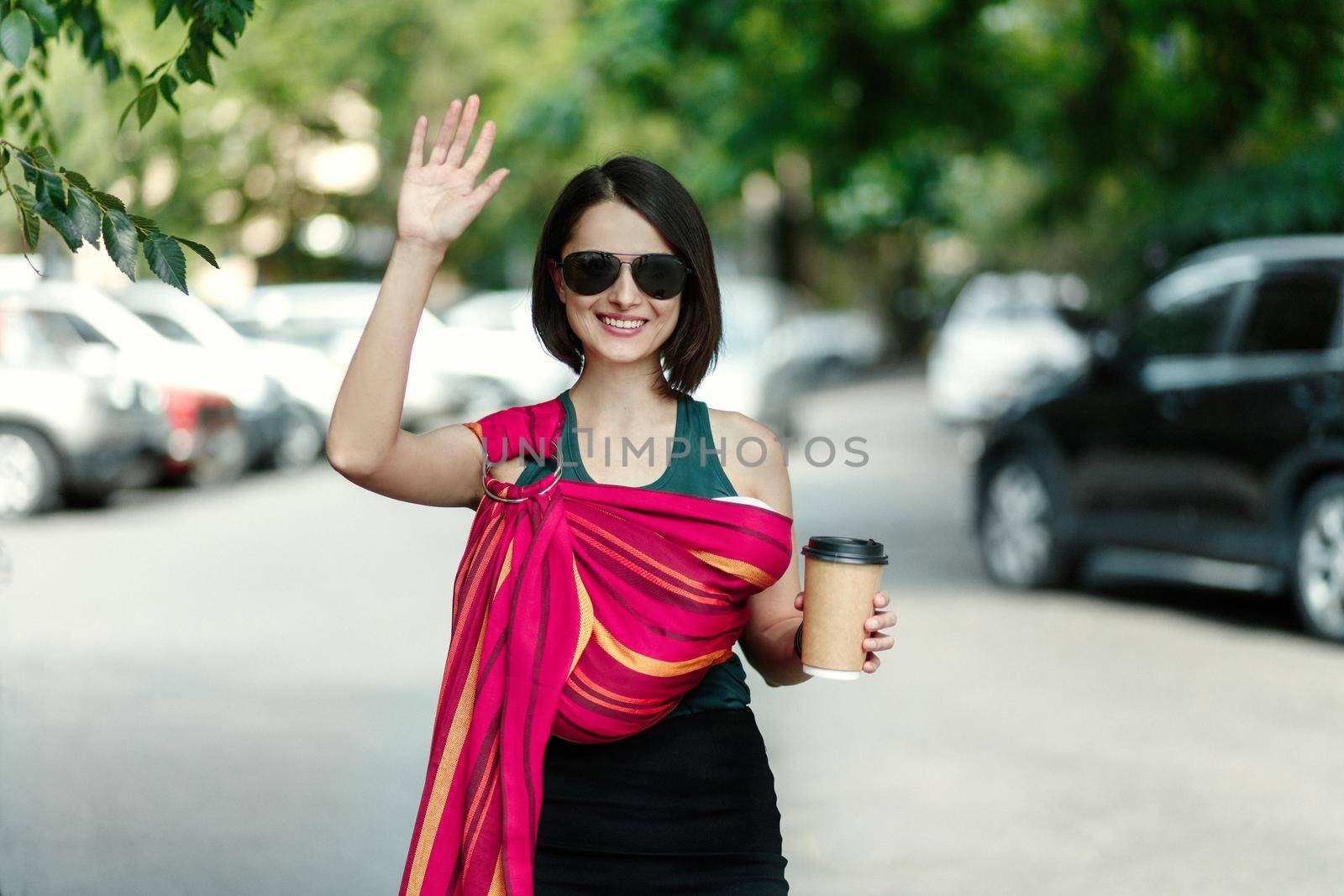 Portrait of trendy woman in sunglasses with baby in sling walking along city. by Rom4ek