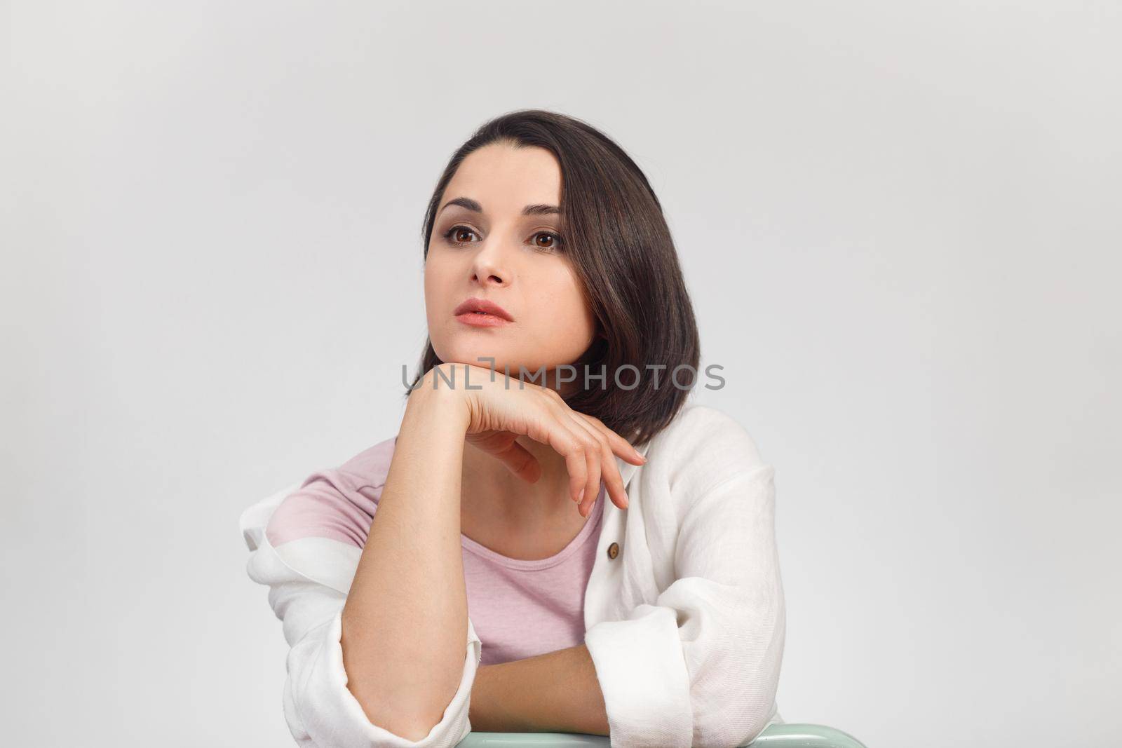 High-key studio portrait of a young dreaming woman in light clothes looking into the distance.