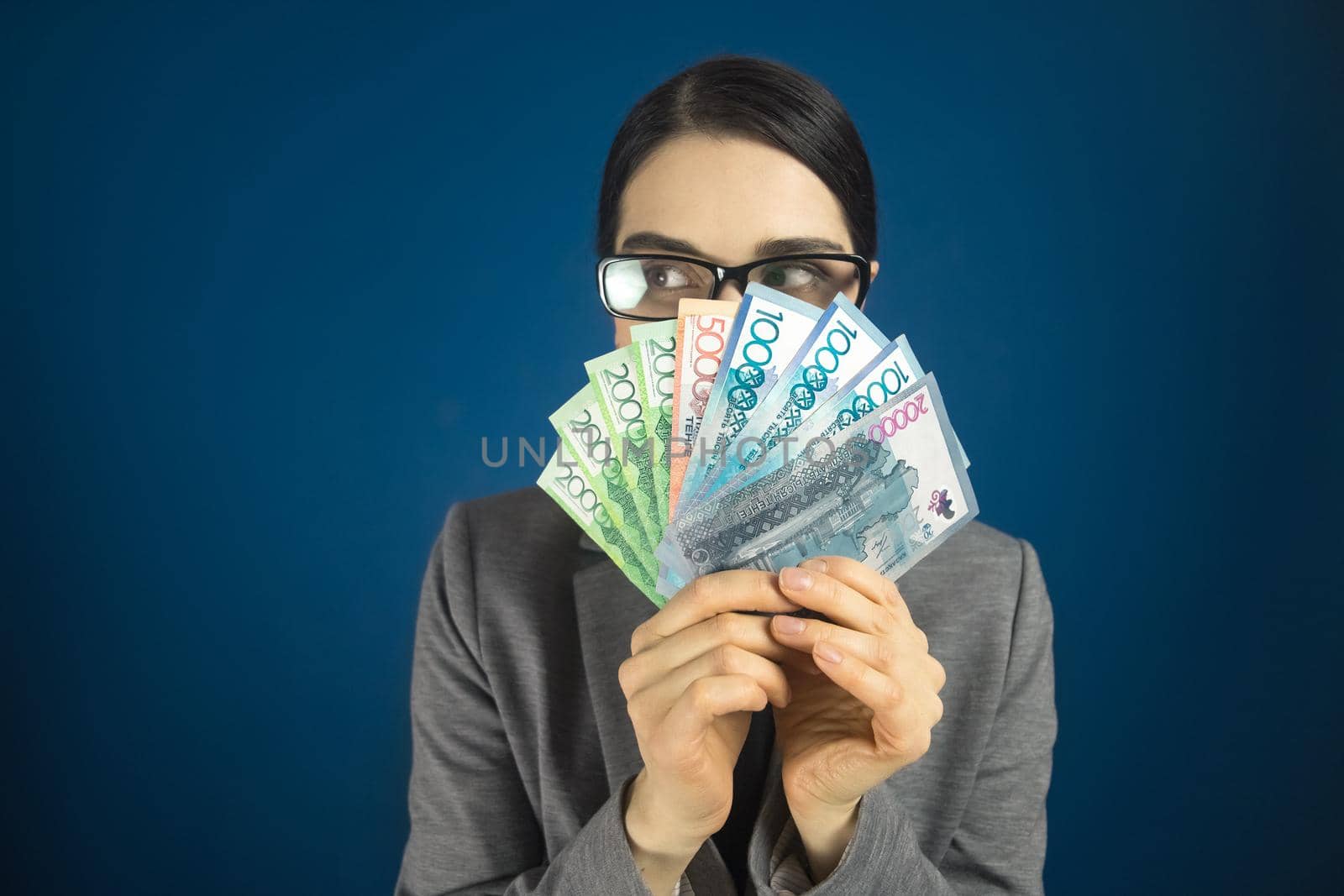 Woman looking sideways above Kazakhstan money tenge in her hands by Rom4ek