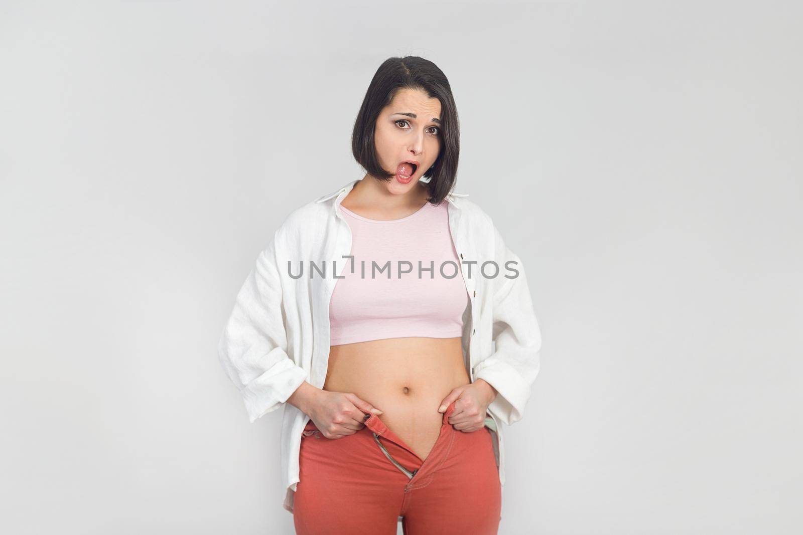 Surprised young woman cannot wear summer pants. Diet, overweight, obesity concept.