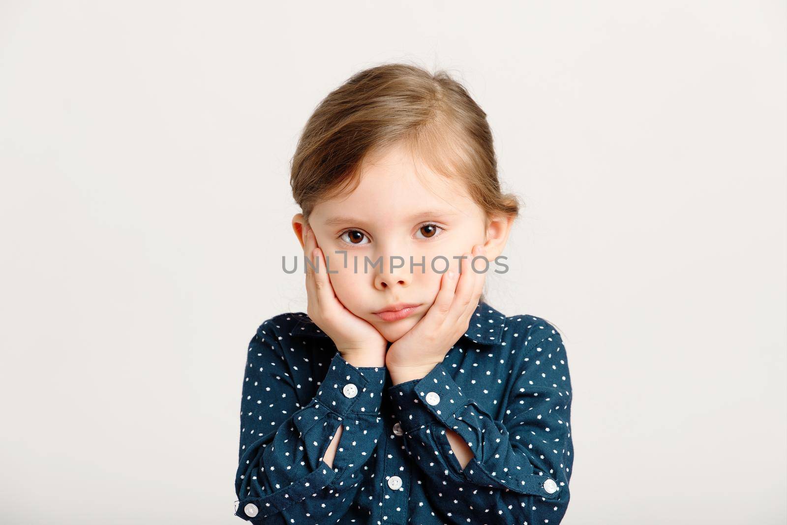 Portrait of an offended, gloomy, angry little girl 4-6 years old wearing a blue dress with polka dots by Rom4ek