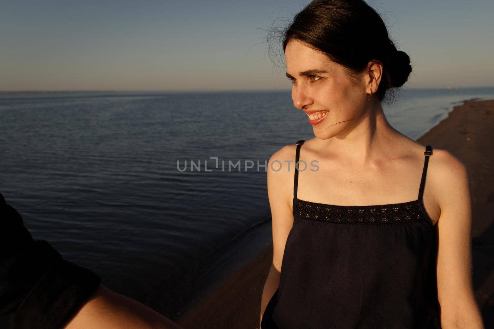 Portrait of a young beautiful woman who looks at her lover off-screen on the background of the sea in the sunset lighting.