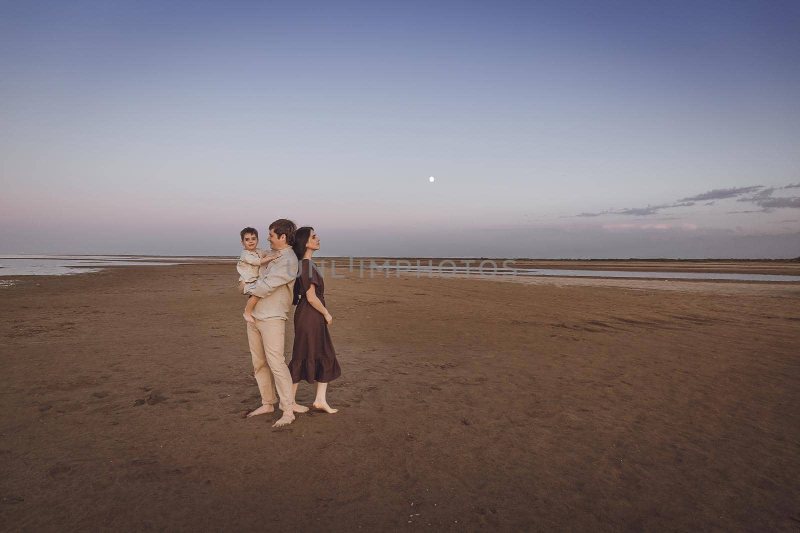 Beautiful young family spend time together walking on the evening beach. Copy space.