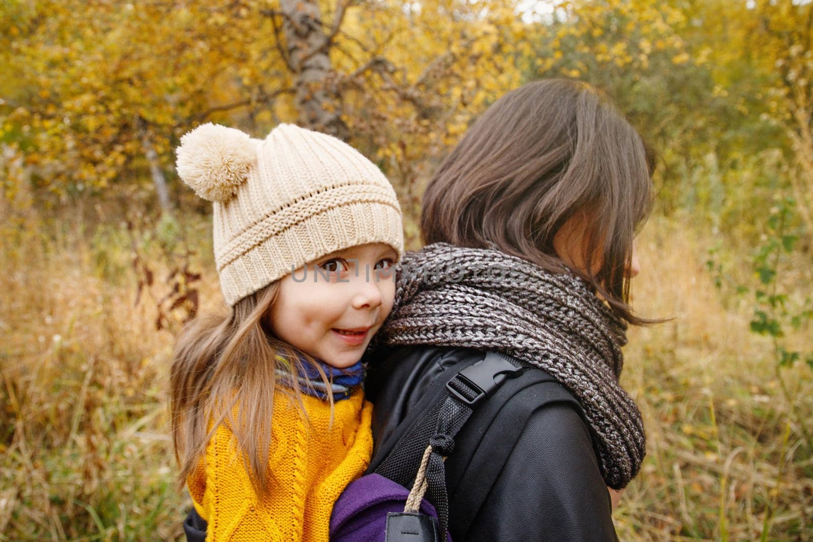 Young mother with her toddler kid girl on back in ergonomic baby carrier in autumn nature. Active mother concept by Rom4ek