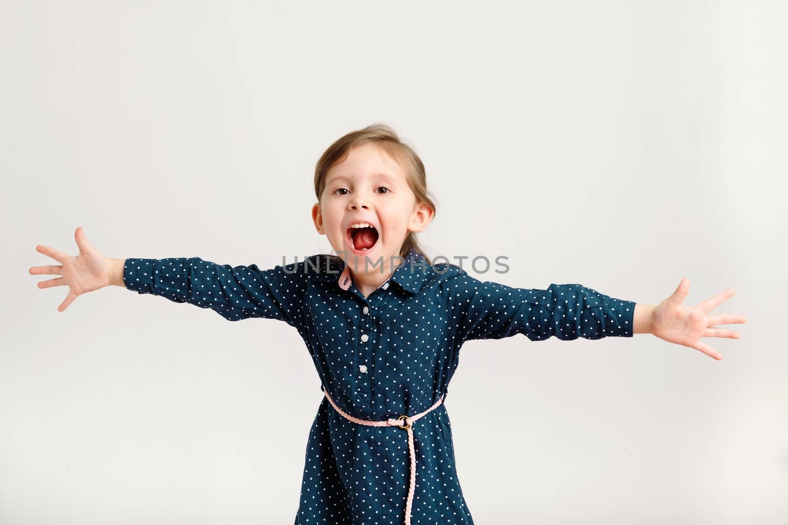 Little cute screaming 4-6 years old wearing a blue dress with polka dots standing with hands in different directions by Rom4ek