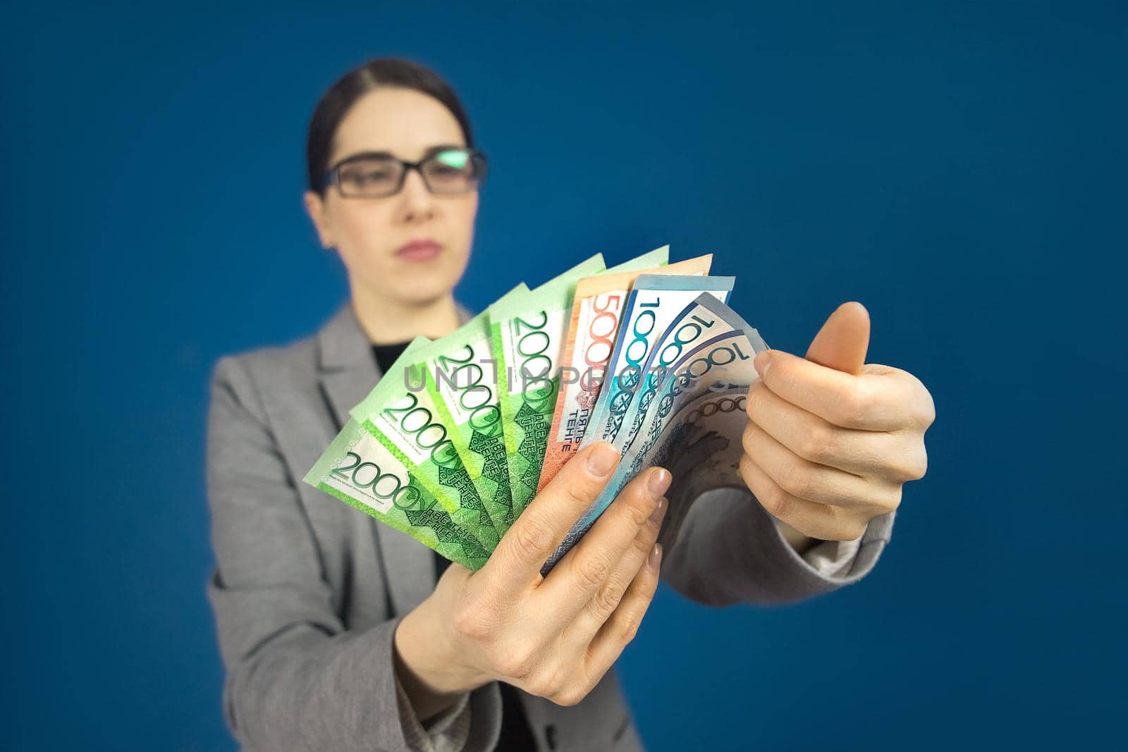 Close-up of various denominations of Kazakhstani tenge bills in the hands of a woman in glasses. Selective focus by Rom4ek
