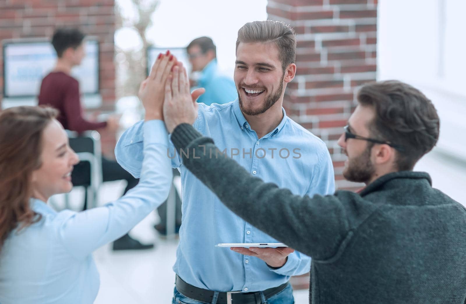Photo of happy young business people holding a tablet and giving high five.