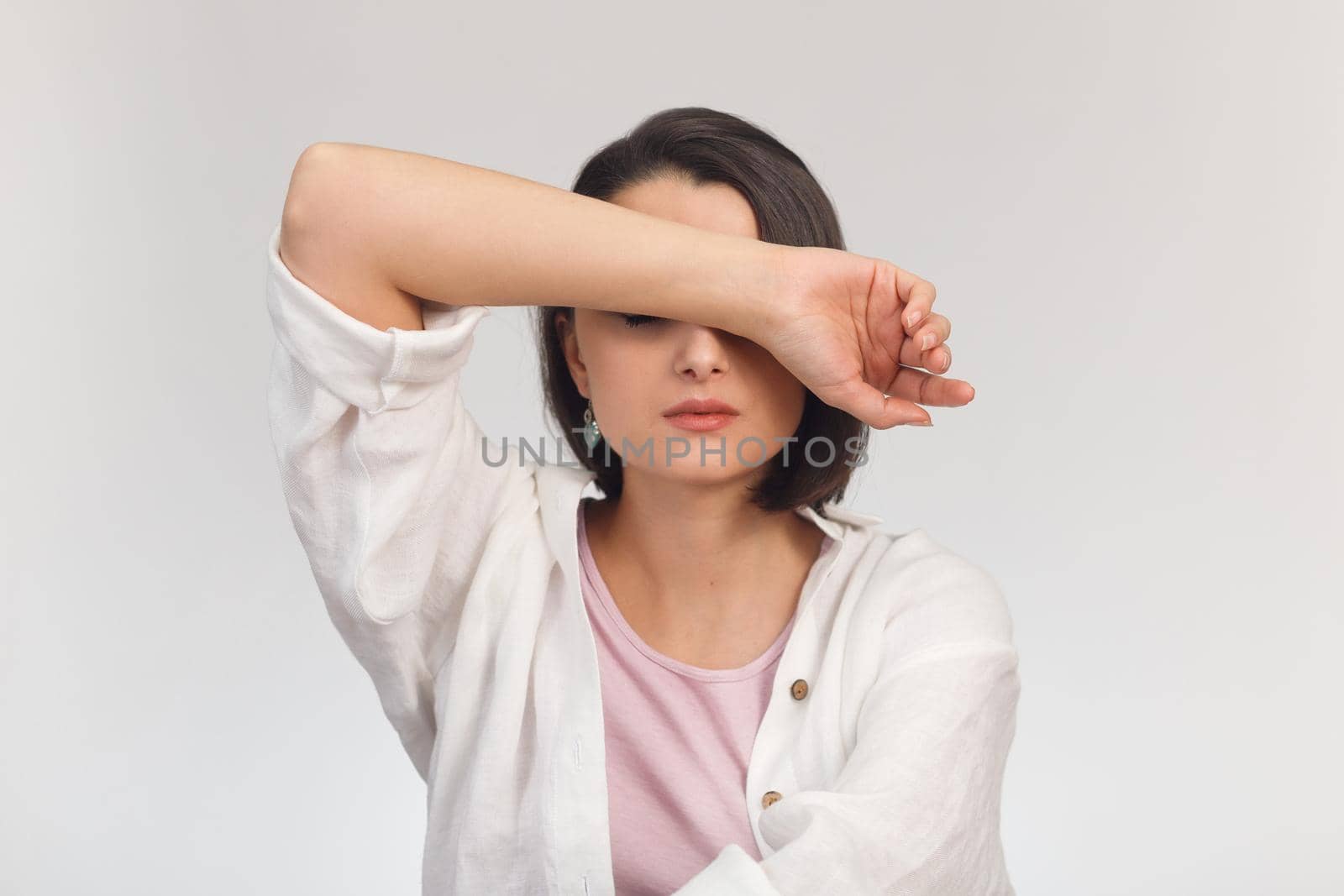 High-key studio portrait of a young woman in light clothes covering her eyes with her hand by Rom4ek