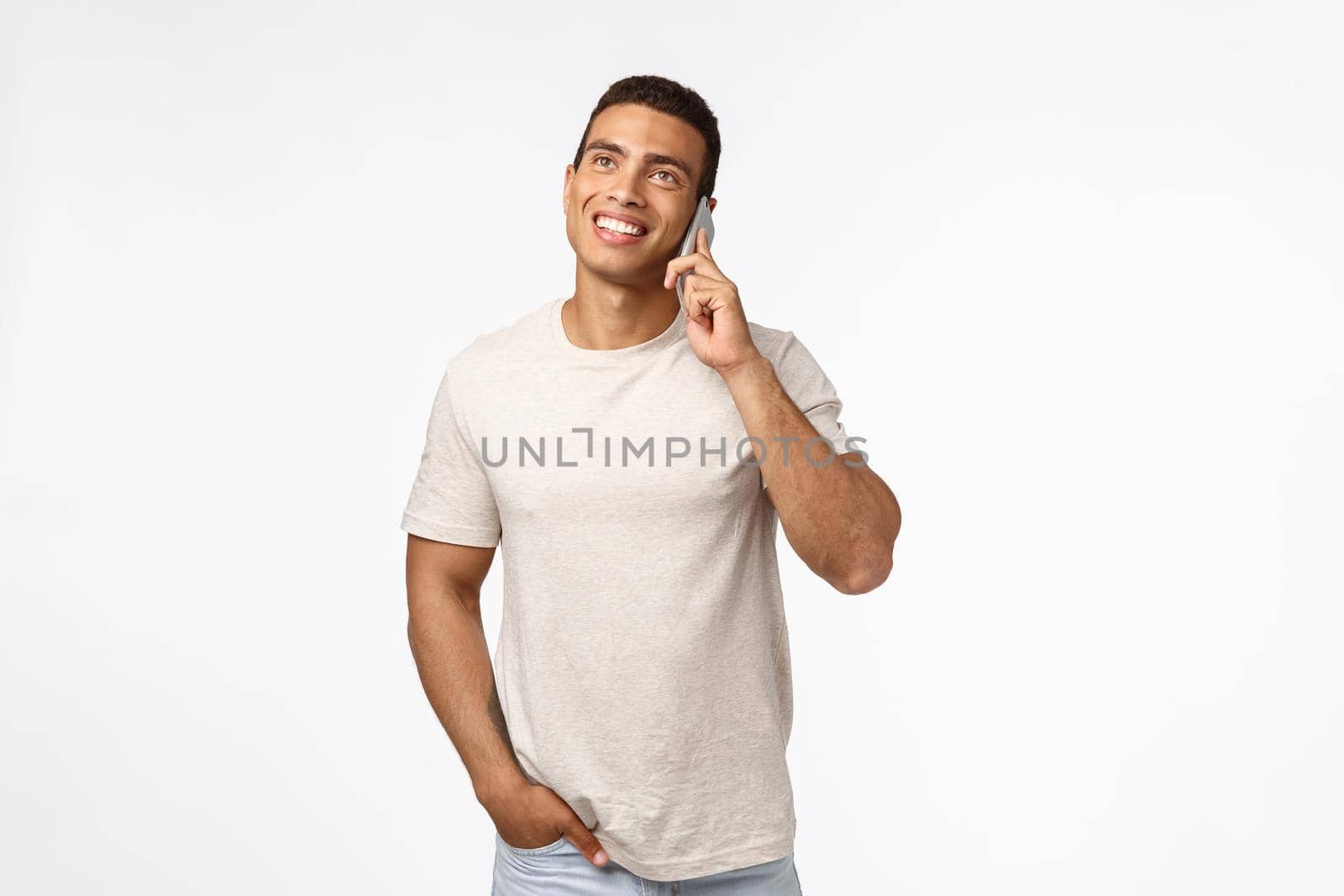 Cheerful, smiling young man in t-shirt, having conversation with friend, looking up enthusiastic, hold hand in pocket casually, smartphone pressed to ear, talking joyfully, white background.