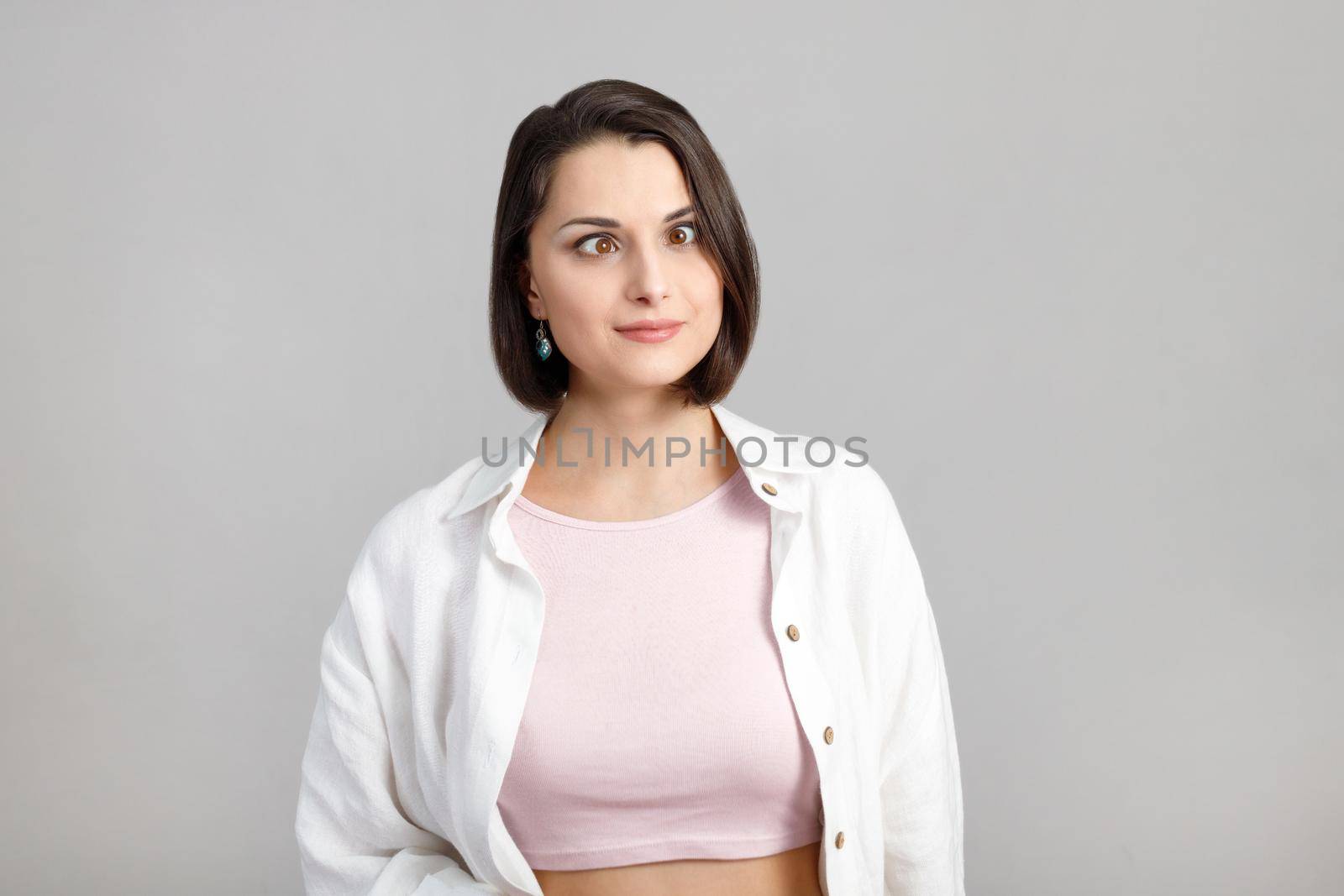 High key portrait of funny brunette multiethnic woman squinted her eyes in pink tank and white shirt.
