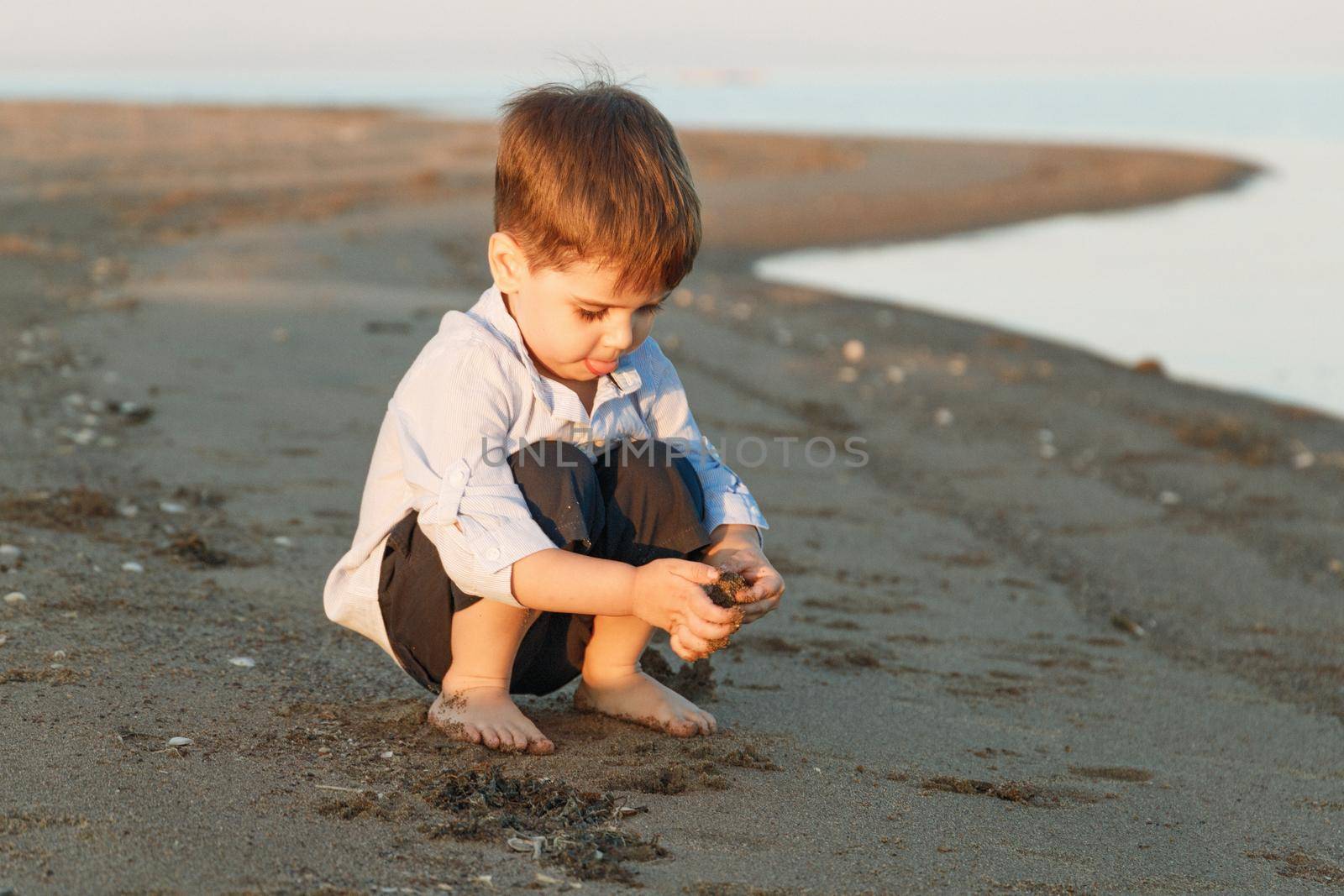 Little cute boy 3 years old plays with sand on the beach in the evening by Rom4ek