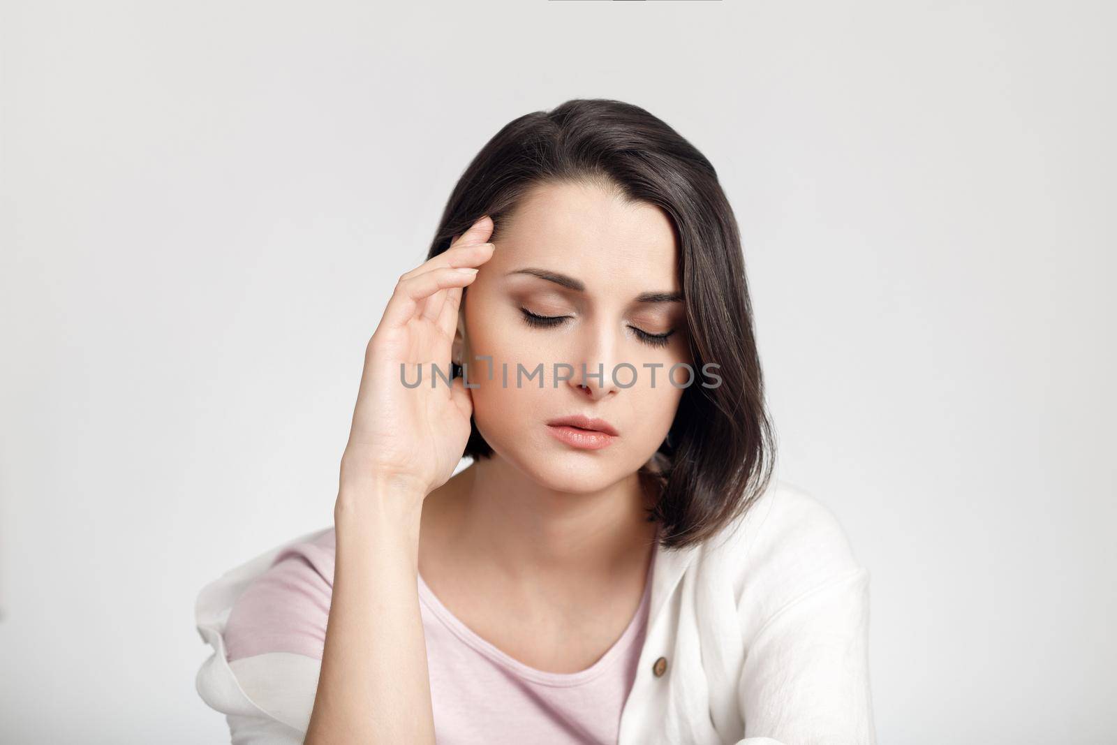 Tired young woman with closed eyes holding her head.