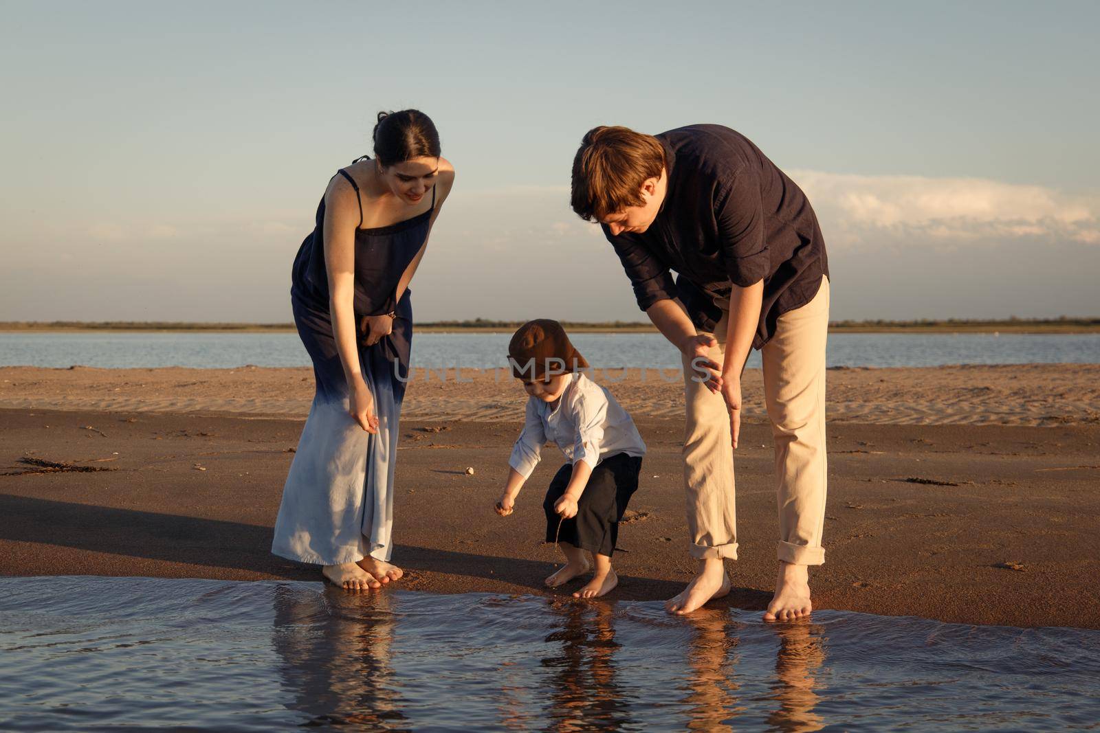 Little boy in brown hat spends time on the beach with his parents.