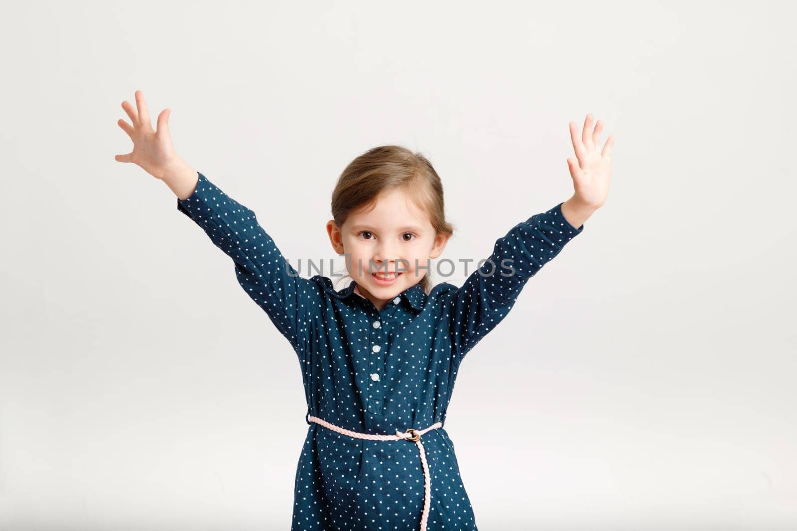 Little cute happy smiling girl 4-6 years old wearing a blue dress with polka dots standing with hand up. Cute kid girl on a white background