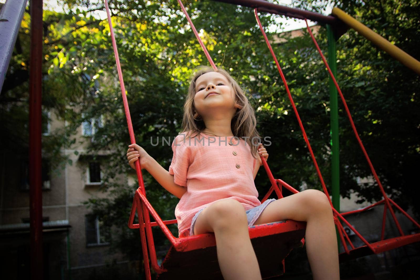 Little happy girl swinging portrait on playground outdoors.