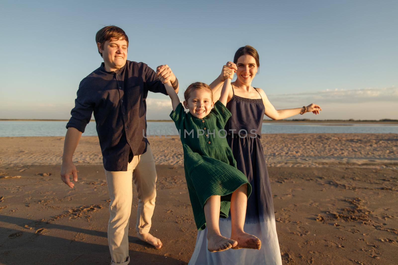 Young family playing with daughter on the evening beach.