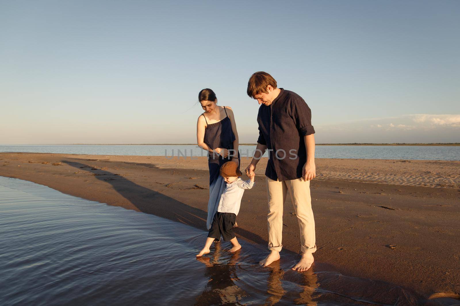 A young family with a three year old son walks barefoot along the wild evening beach.