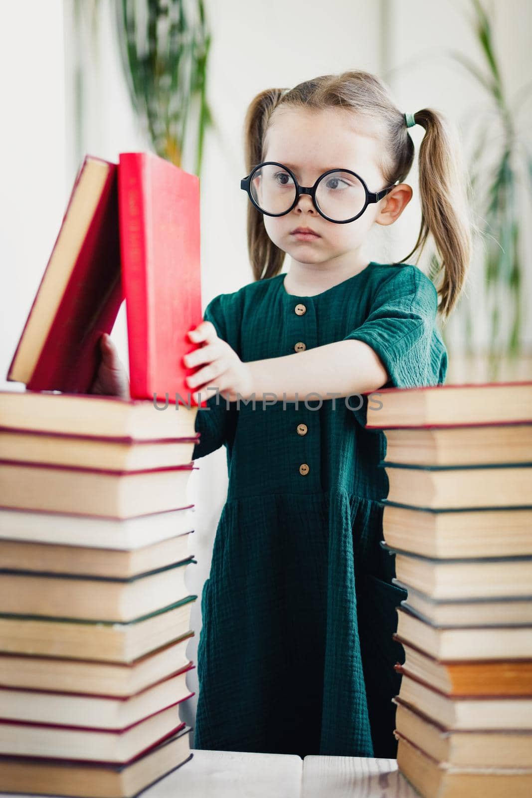 Caucasian little child girl in green dress and glasses procrastination while reading book. Home work and preschool education concept