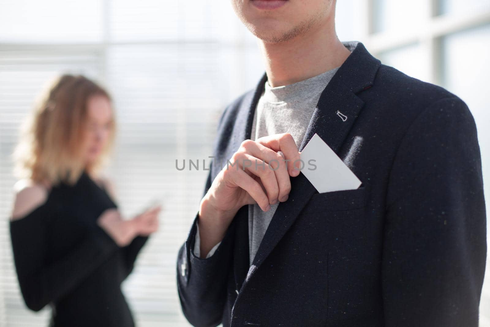 Young business man holding white business card on modern office blur background.