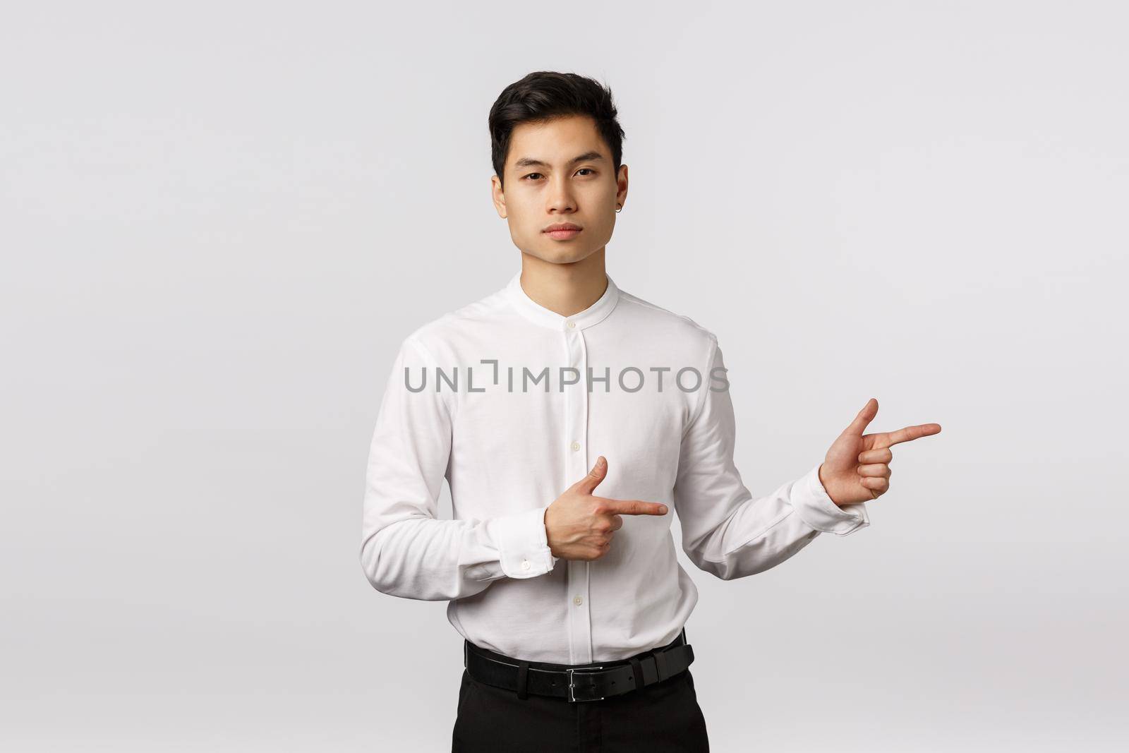 Serious-looking sassy and handsome asian millennial guy in formal wear, shirt and pants, pointing right, looking camera assertive, employer give direction, offer product, white background.
