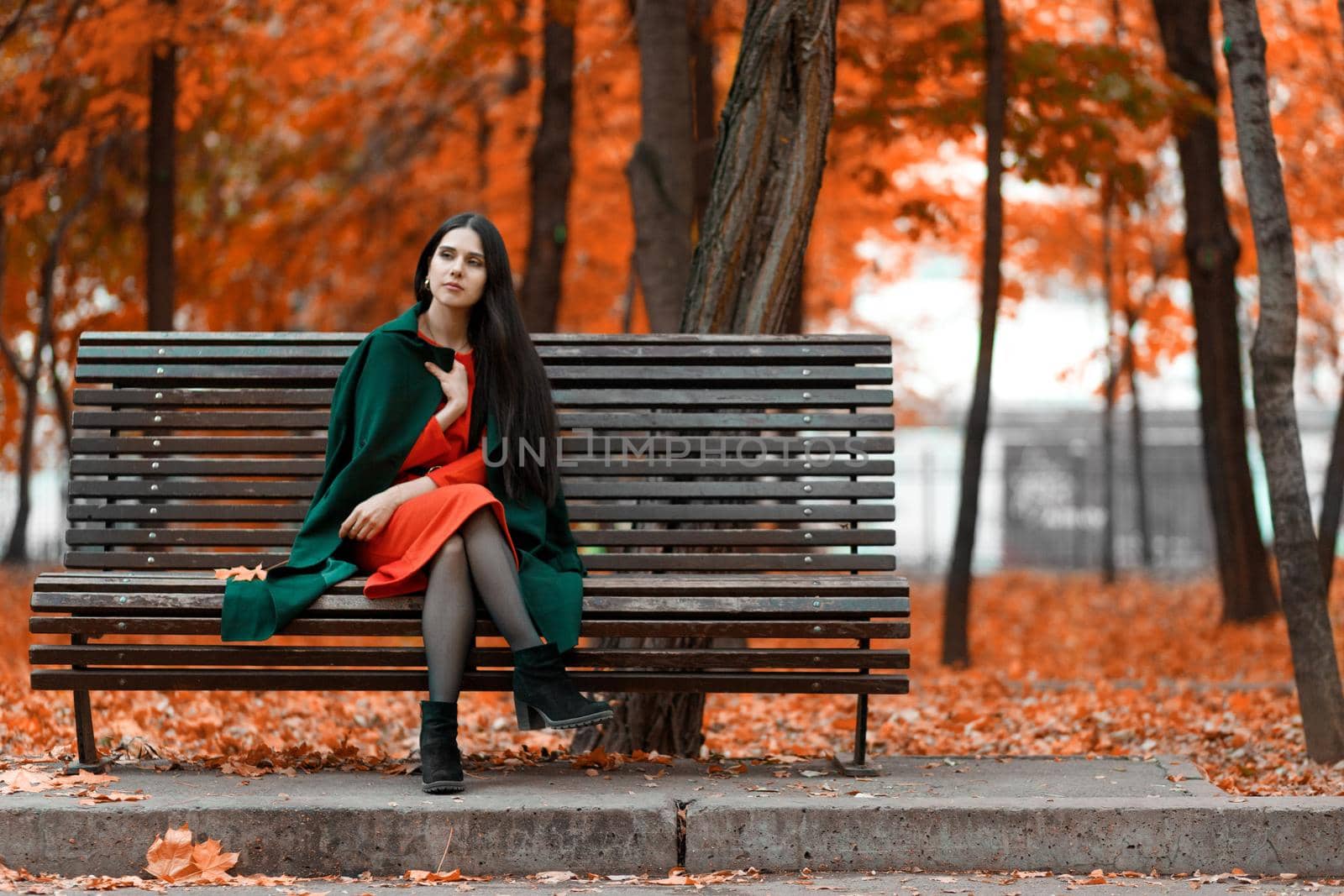 Young beautiful brunette bored alone on a bench in an autumn park.