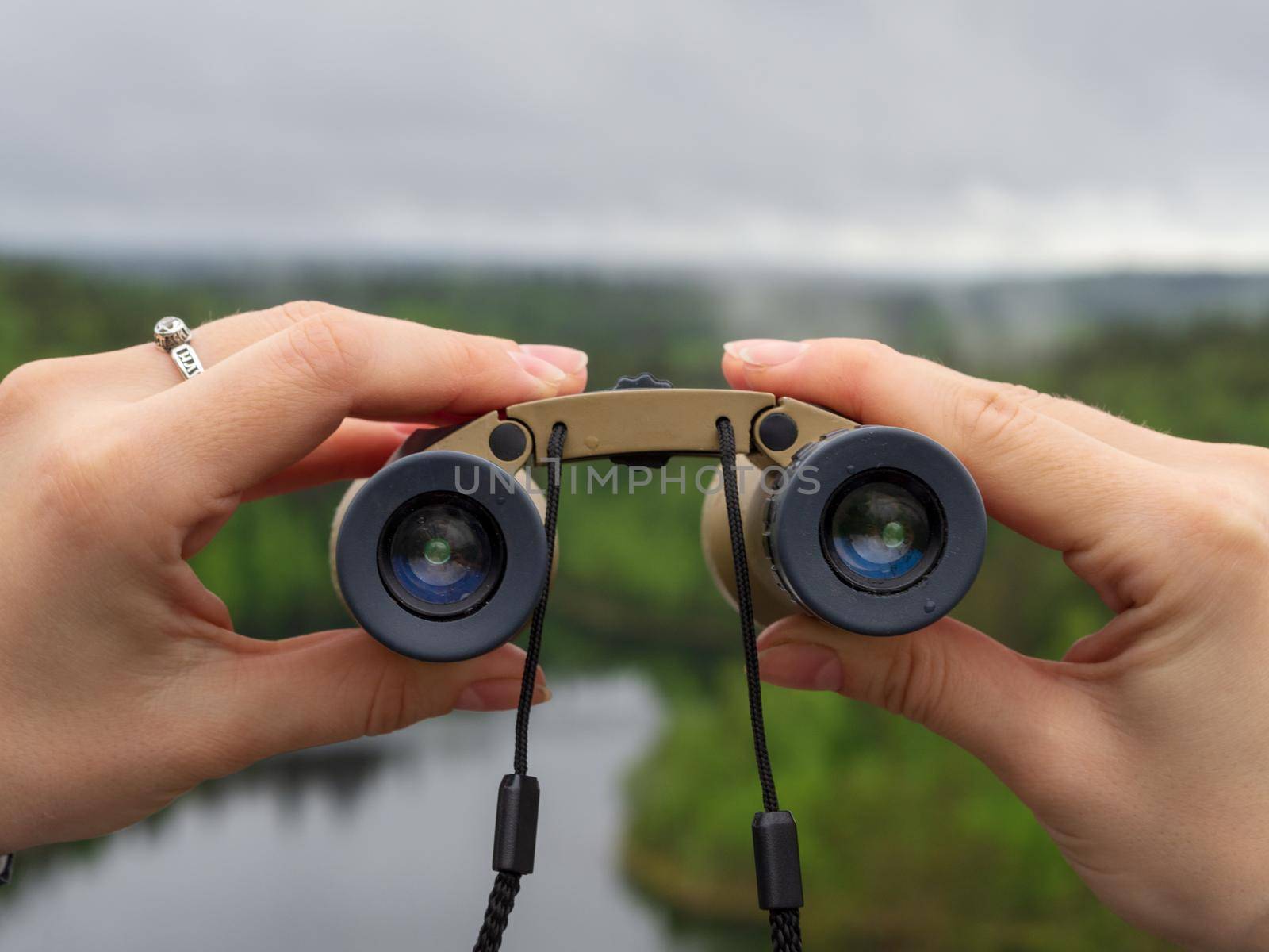 woman looks through binoculars. tourist girl on a rock in a forest near a lake