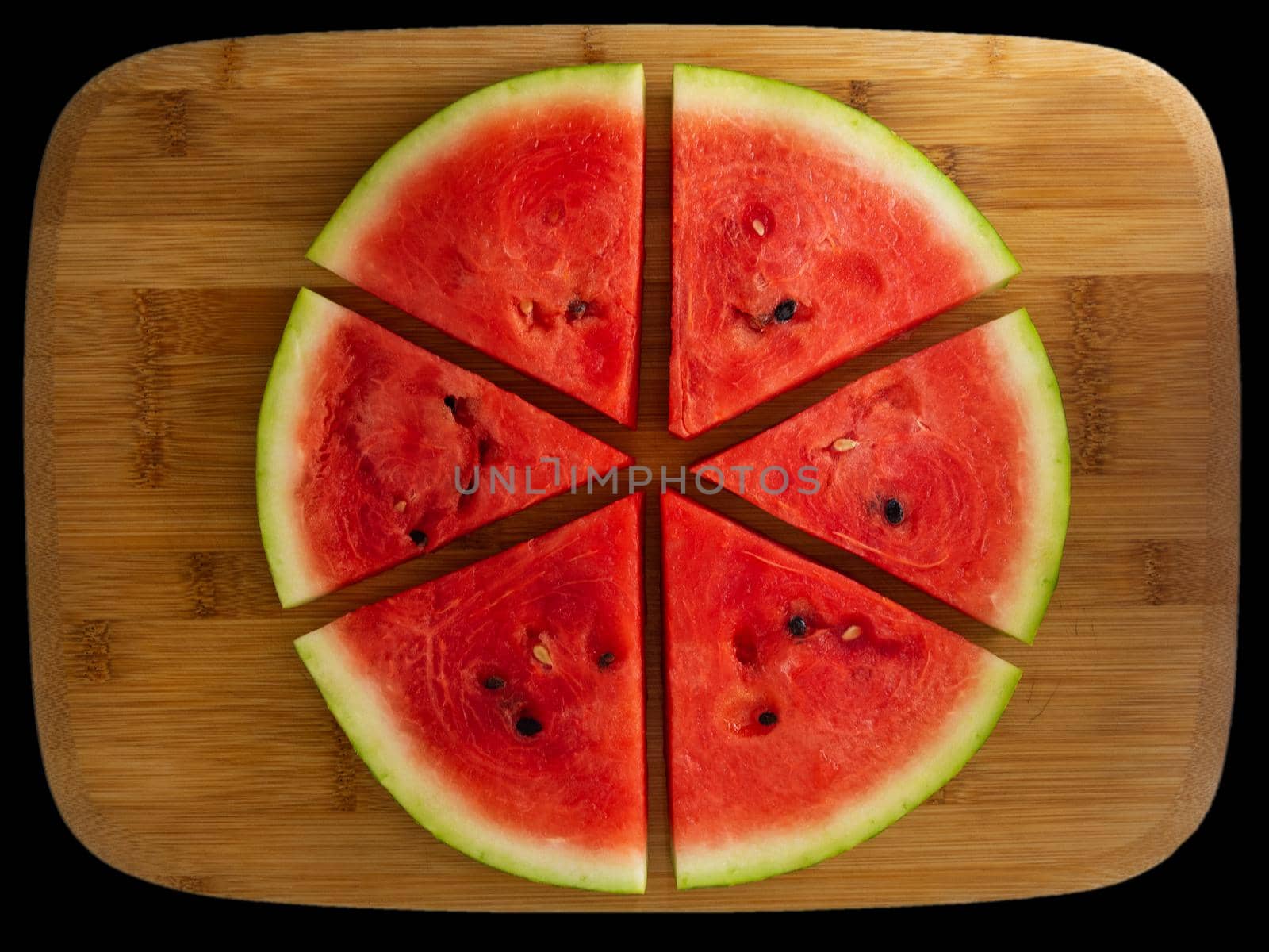 Slices of fresh red tasty watermelon laid out in a circle on a wooden background.