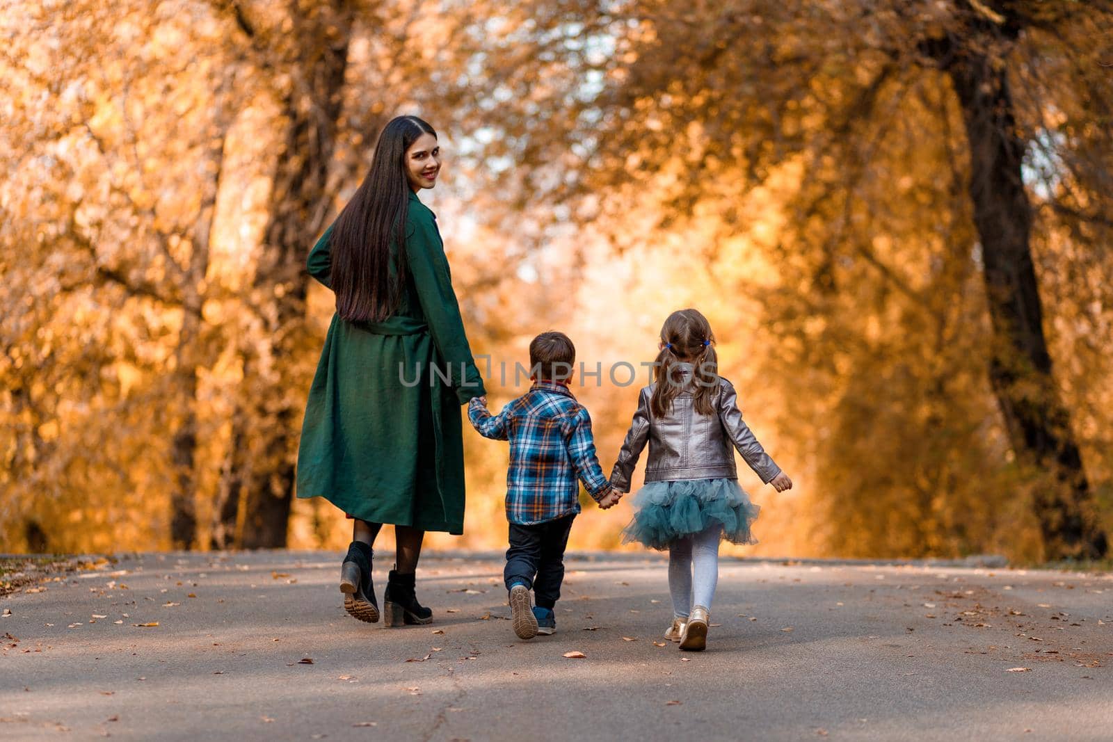 Young beautiful mother with two children is walking in the autumn park.