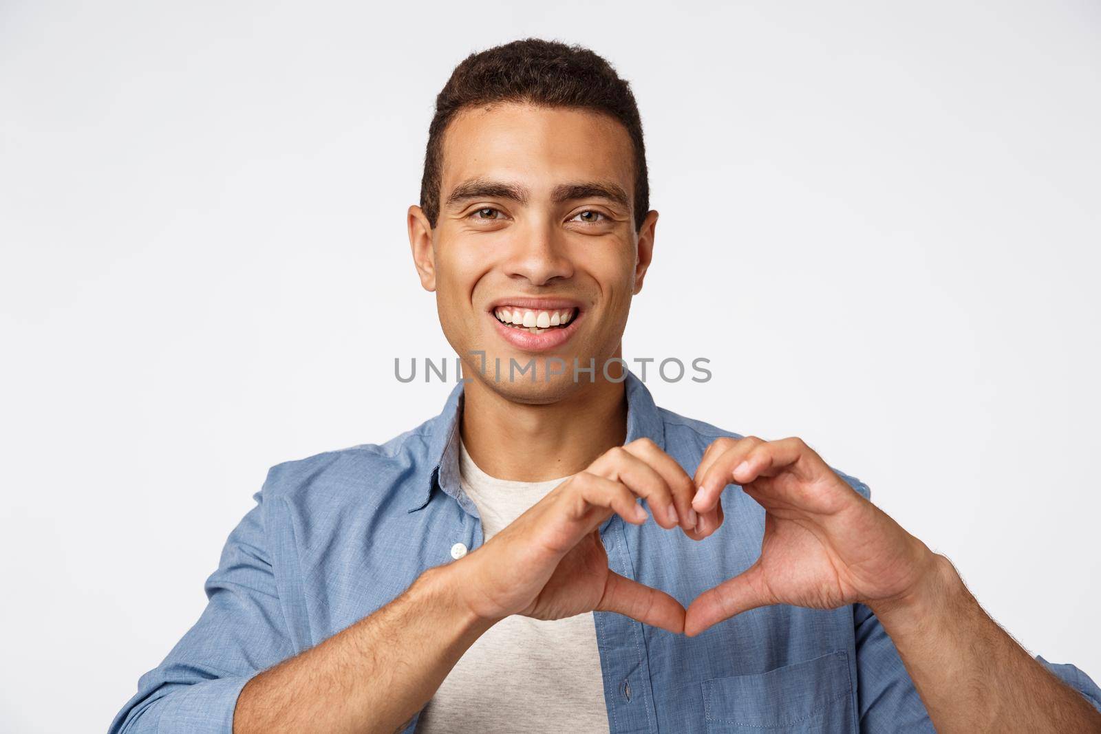 Love, cherity and affection concept. Charming young brazilian masculine man showing heart sign and smiling happy, make surprise dinner for valentines day, arrange christmas romantic night.