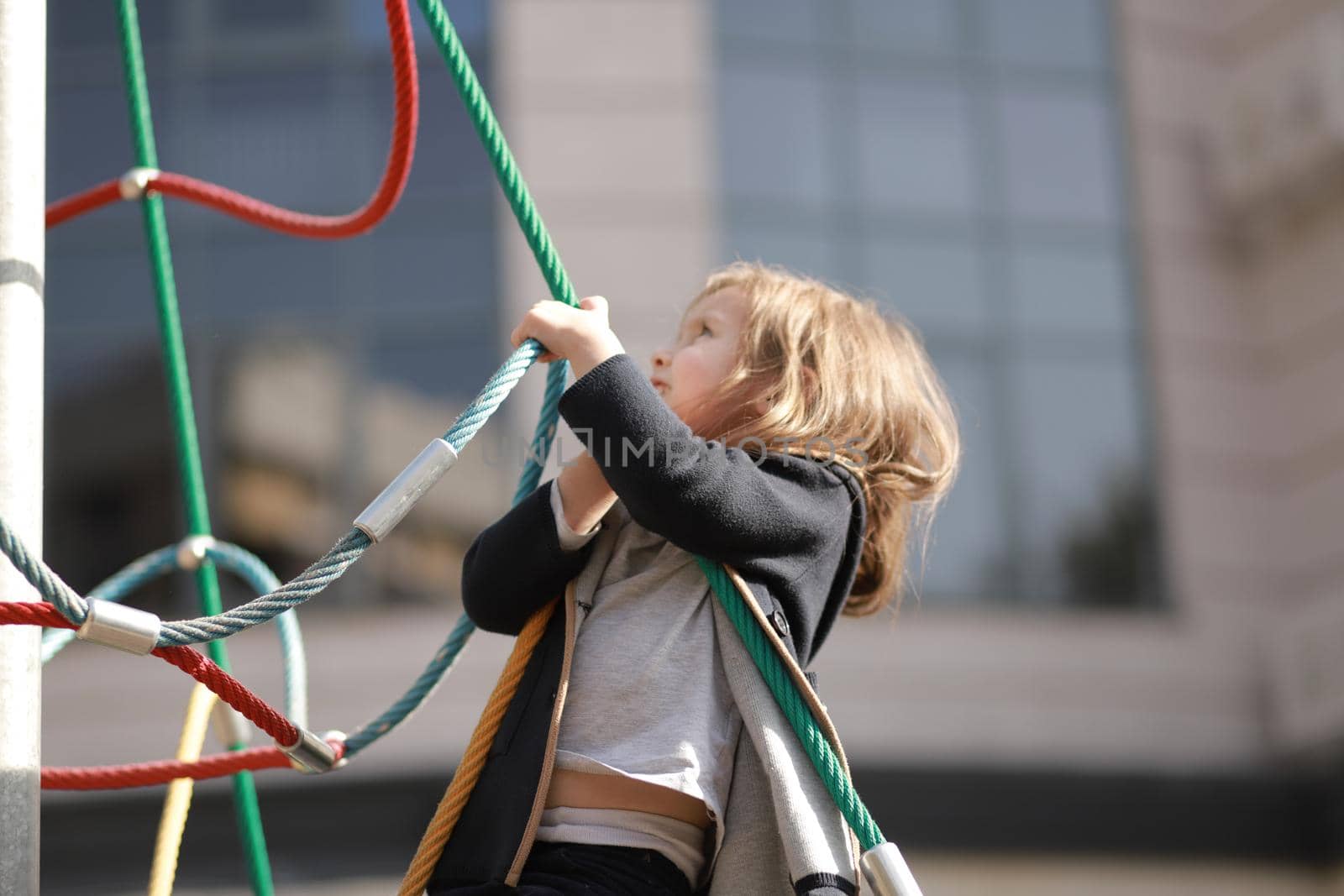 Cute little girl 3 - 5 years old at the urban playground on the background of a modern condominium. Selective soft focus.