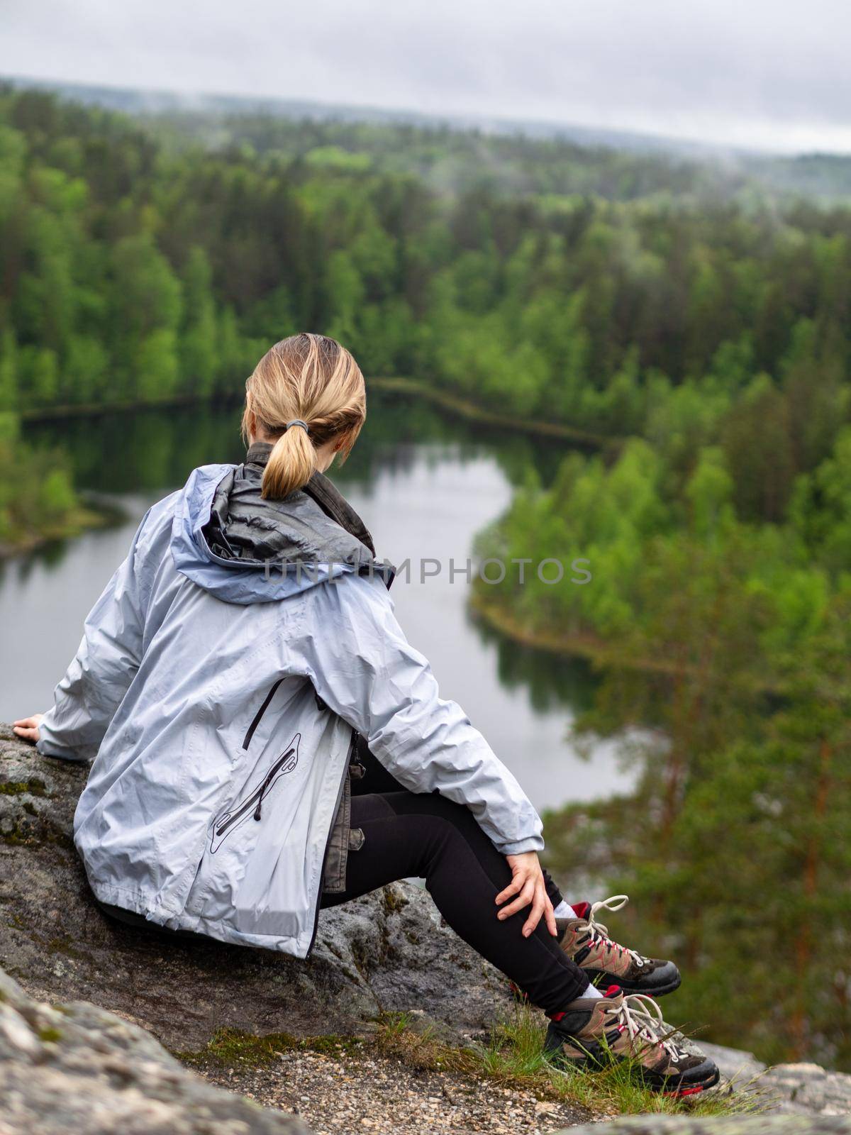 woman looks through binoculars. tourist girl on a rock in a forest near a lake