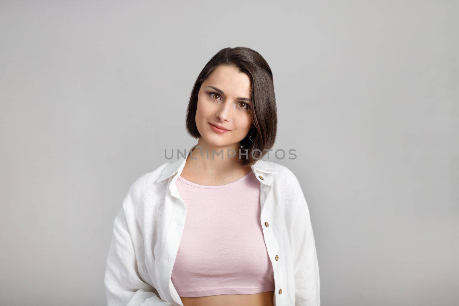 High key calm portrait of young brunette mixed race woman in pink tank and white shirt looking at camera.