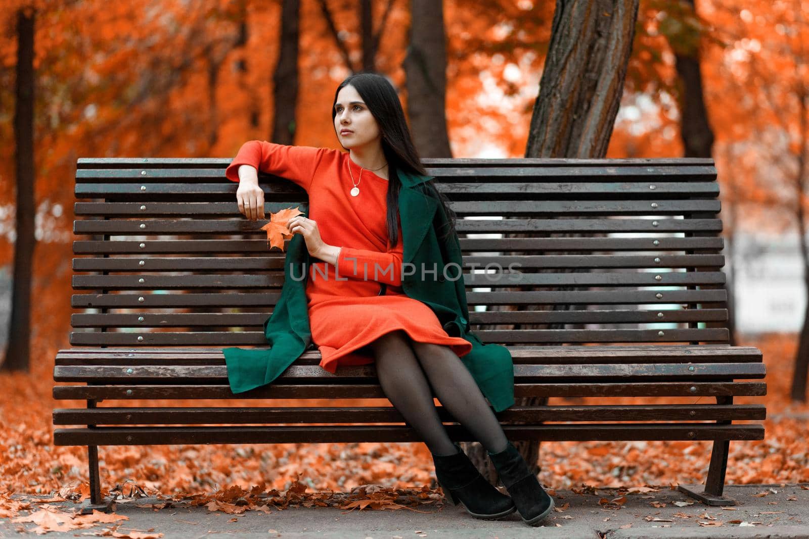 A beautiful young woman is waiting for her boyfriend on a bench in an autumn park. The guy is late.
