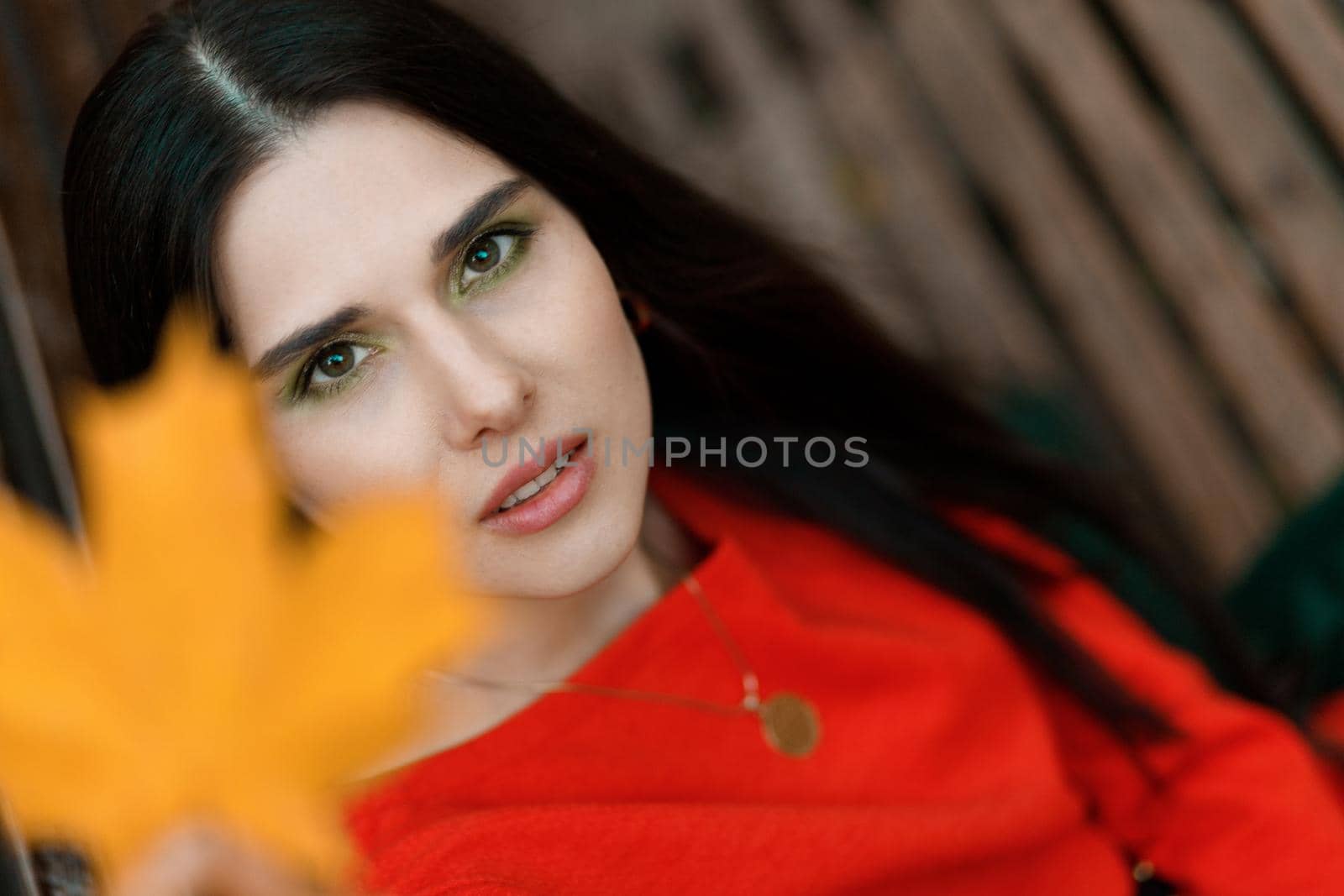 Portrait of a young woman in an orange dress with a yellow autumn leaf out of focus. Autumn tones and mood.