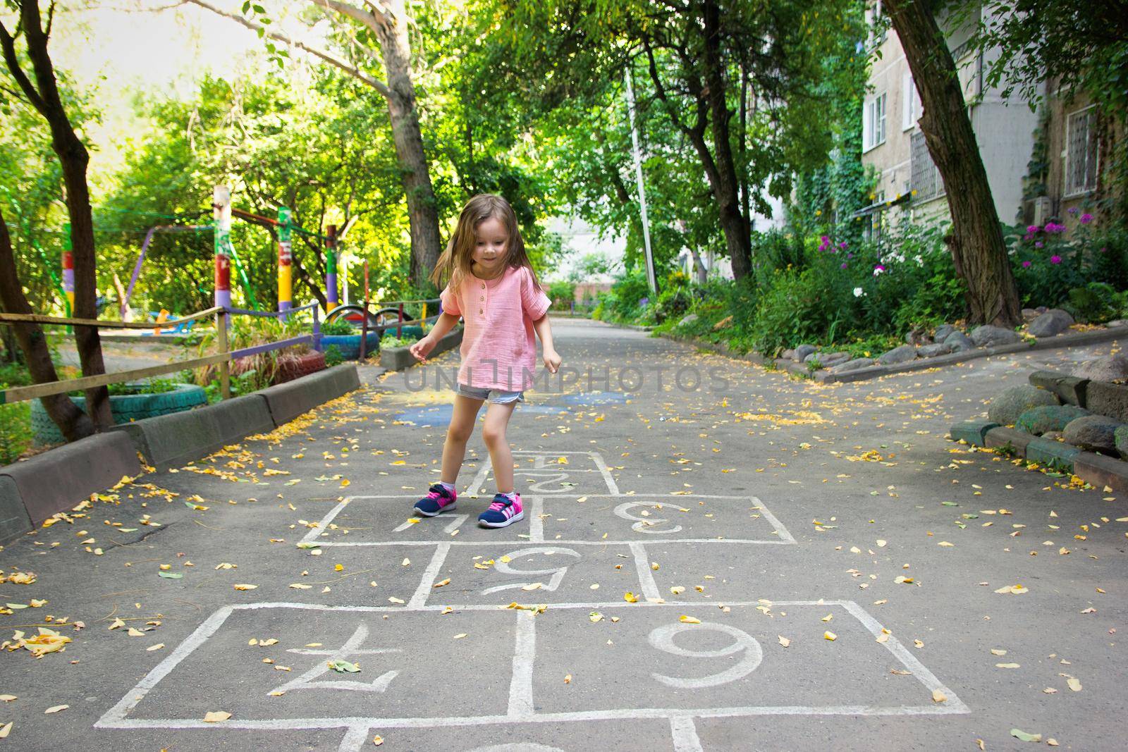 Little cute girl 4 y.o. playing hopscotch on playground outdoors. Lifestyle kid portrait outdoor.