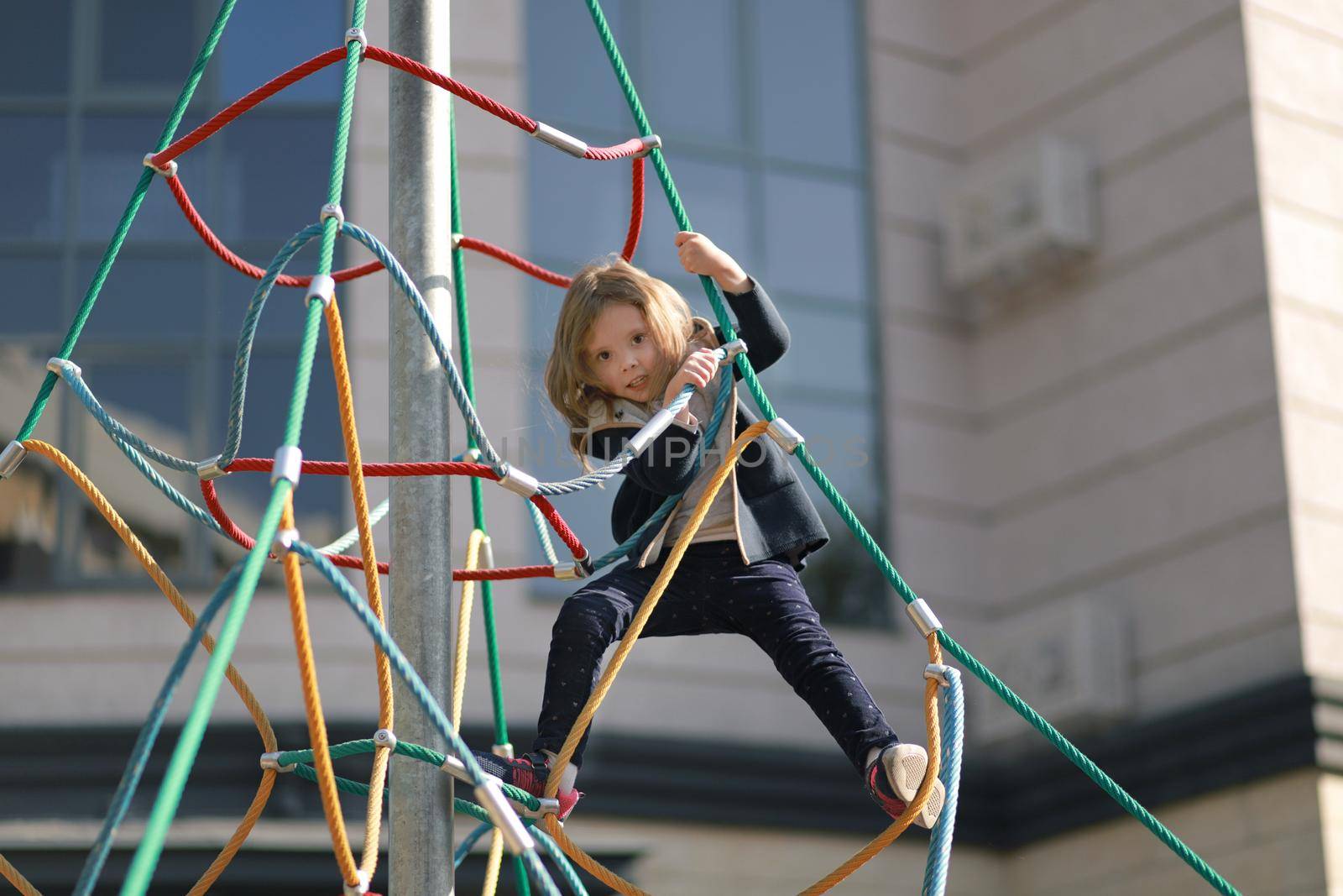 Full of emotion 3-4 years girl playing on the playground on the background of a modern condominium. Selective soft focus.