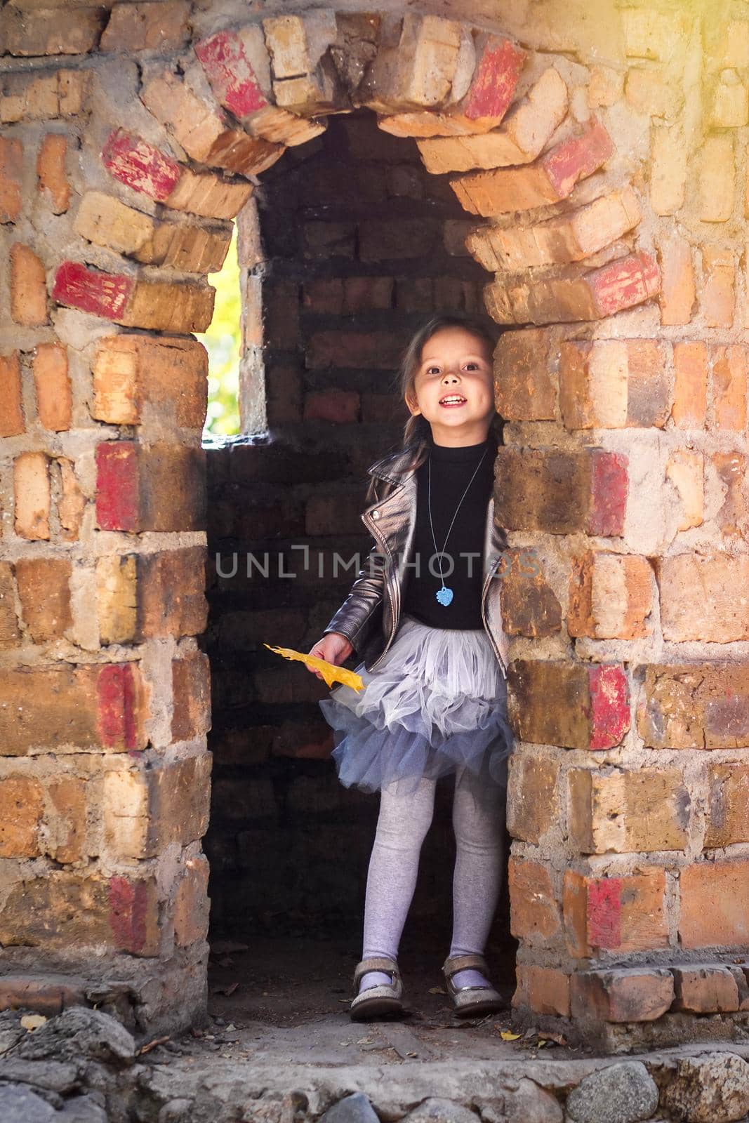 Little cute girl in trendy autumn clothes playing in the tower of the stone castle.