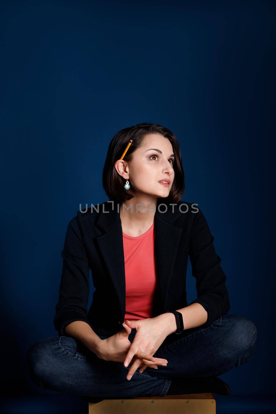 Vertical portrait of a young woman blogger or copywriter with a pencil behind her ear ponders new ideas on blue background.