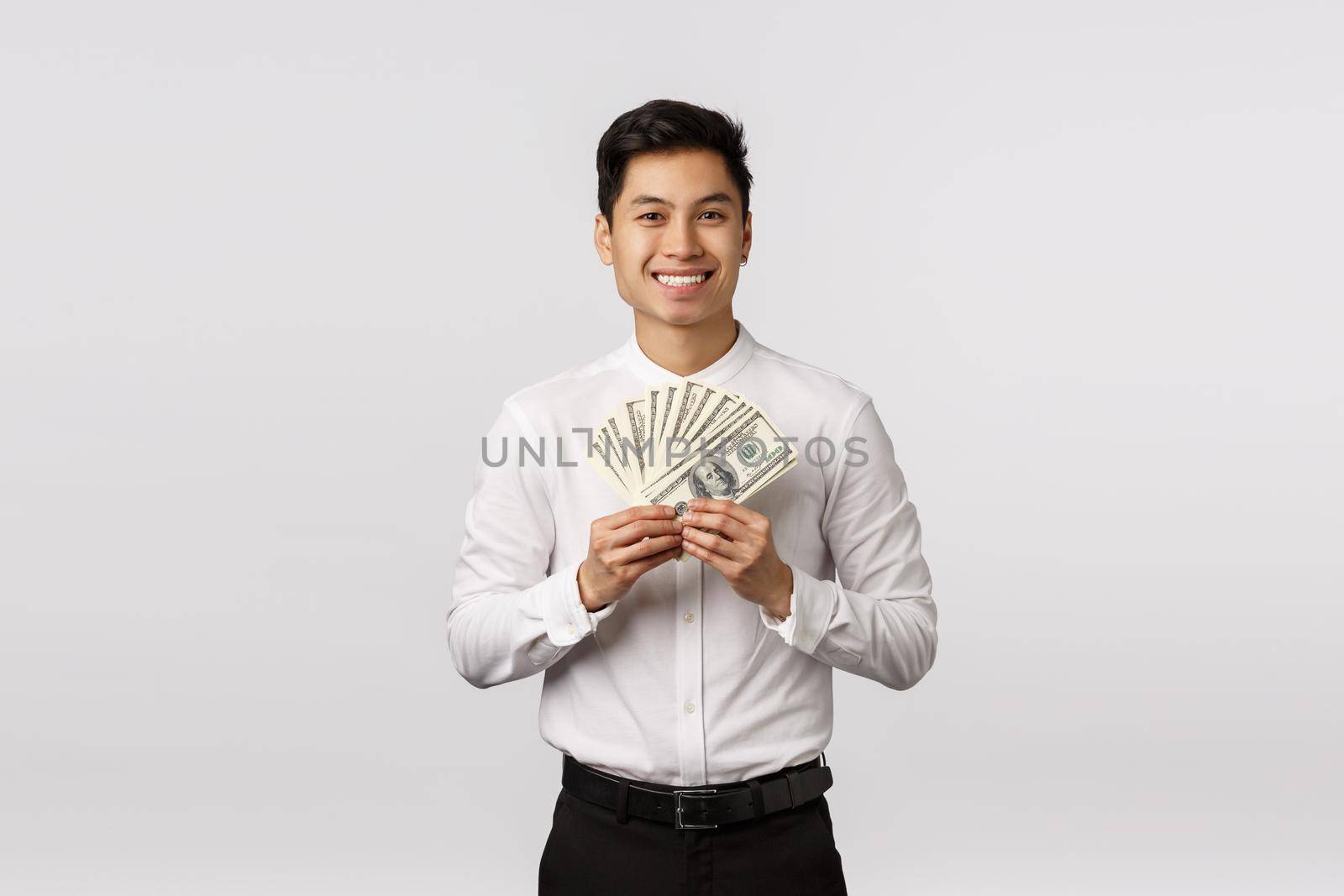 Look at that cash. Handsome happy and rich young asian guy ready spend paycheck on shopping, holding money and smiling, winning sport bid, achieve success corporate ladder, white background.