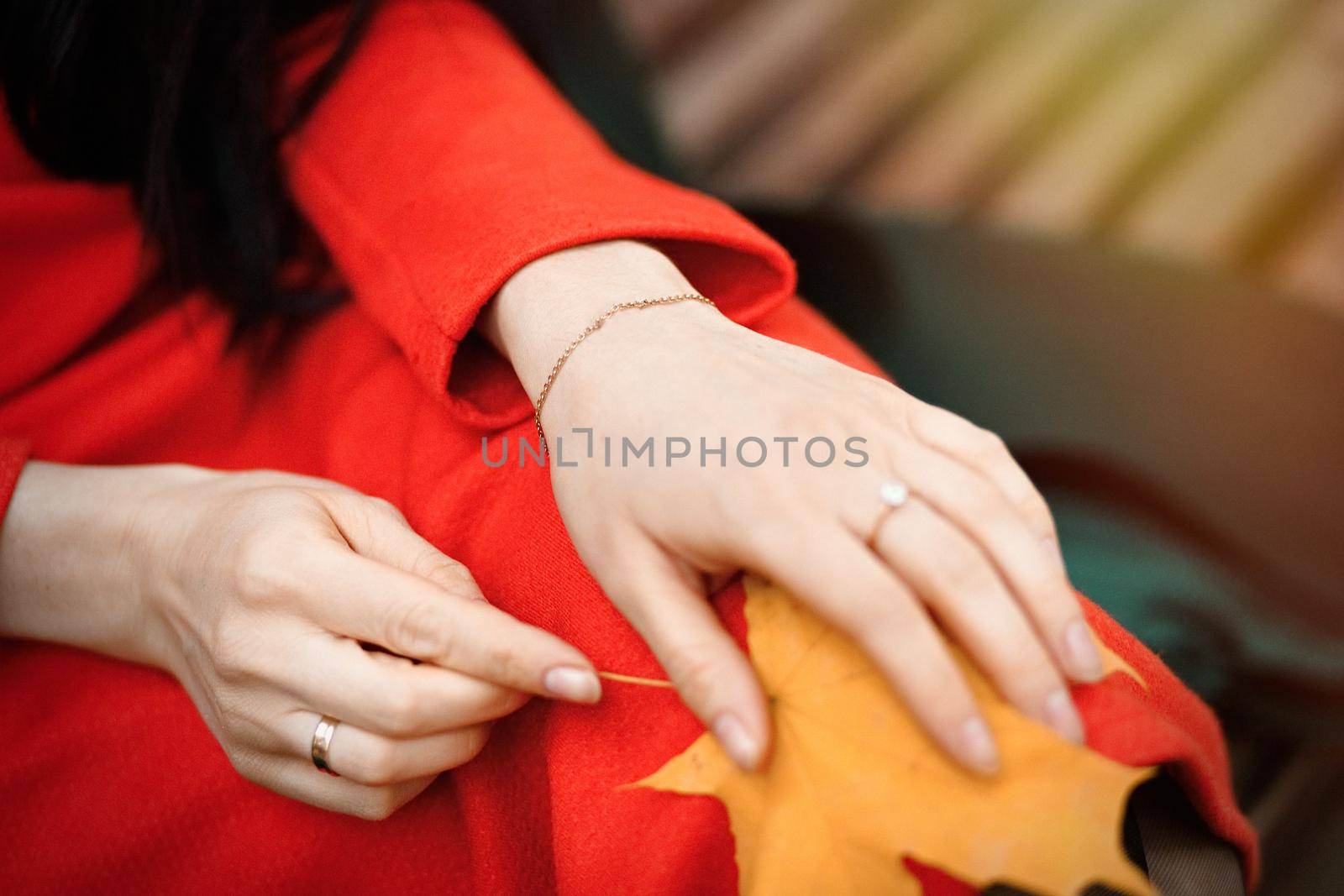 Close-up female hands with bracelet and rings with yellow autumn leaf on the knees.