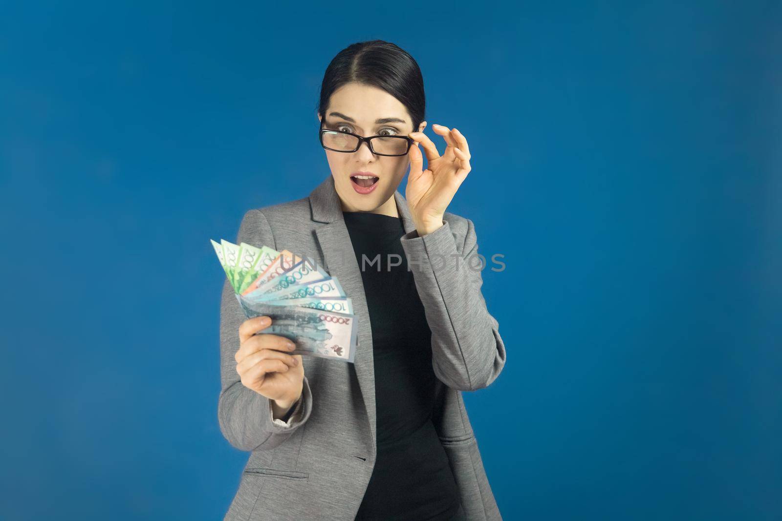 Young beautiful woman looks surprised at a pack of tenge in her hand. Selective focus.