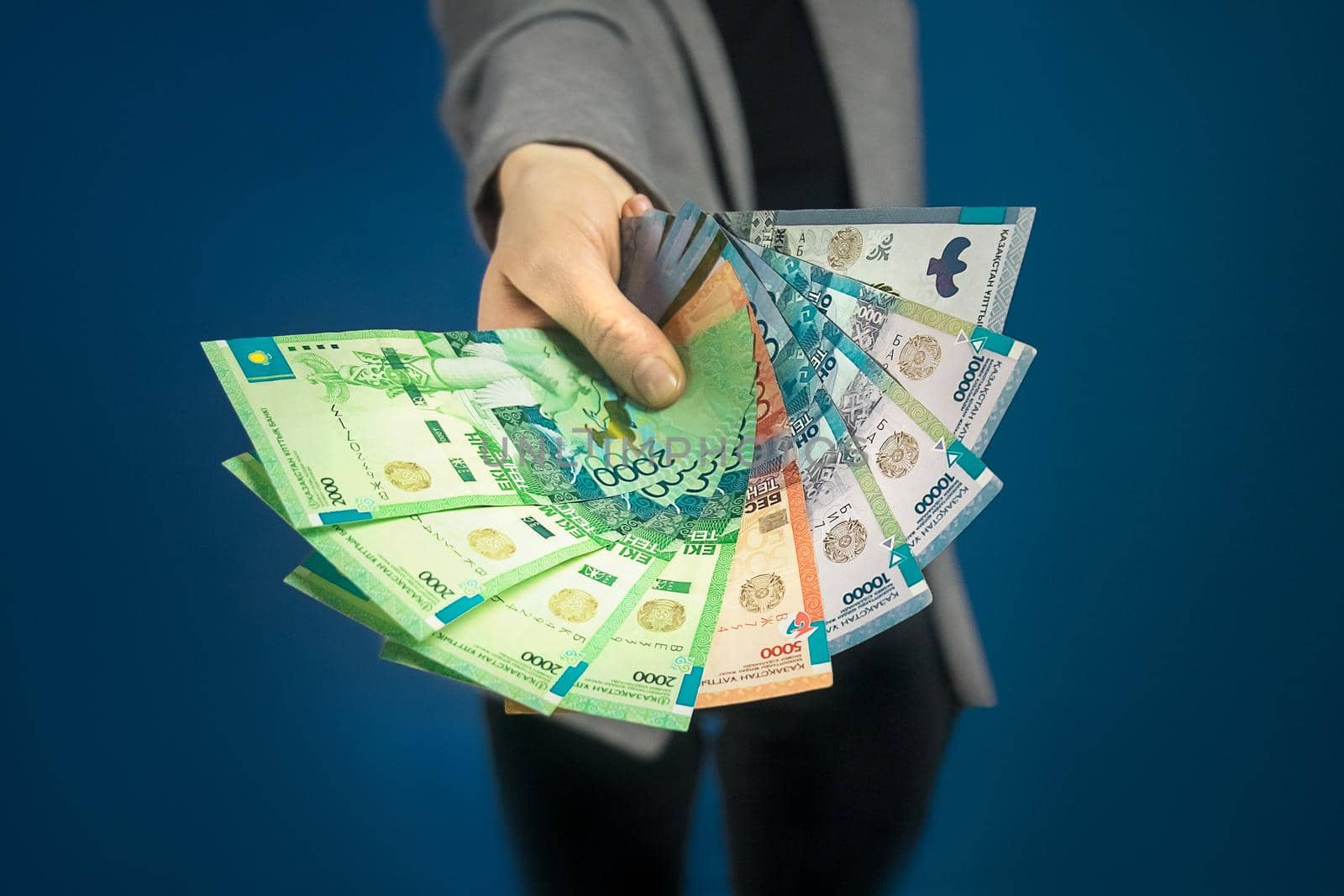 Close-up of tenge in woman's hand on blue background. Selective focus.